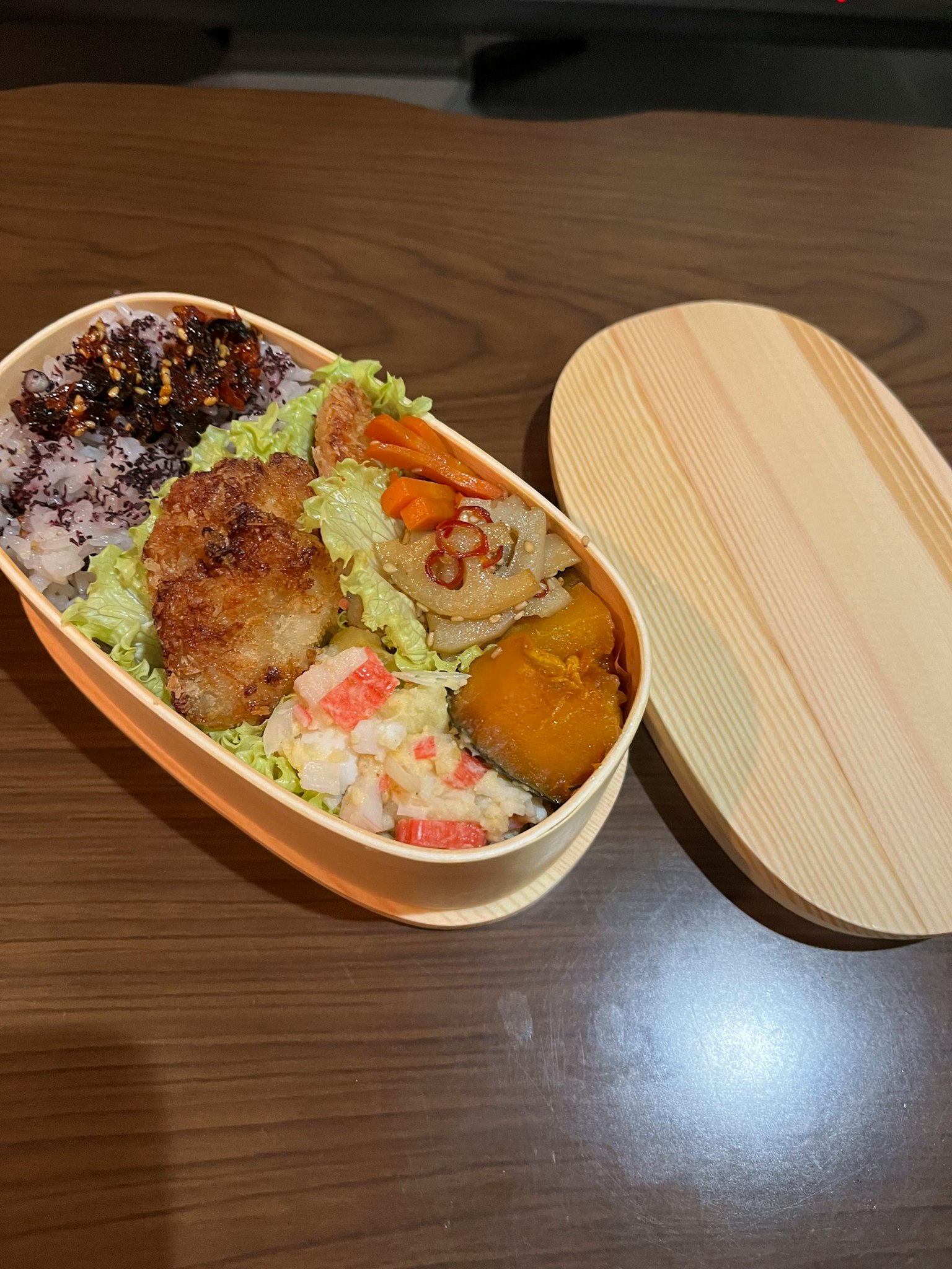 Une boîte à bento remplie de divers plats comprenant du riz blanc du riz noir des crevettes du poulet et une croquette de citrouille