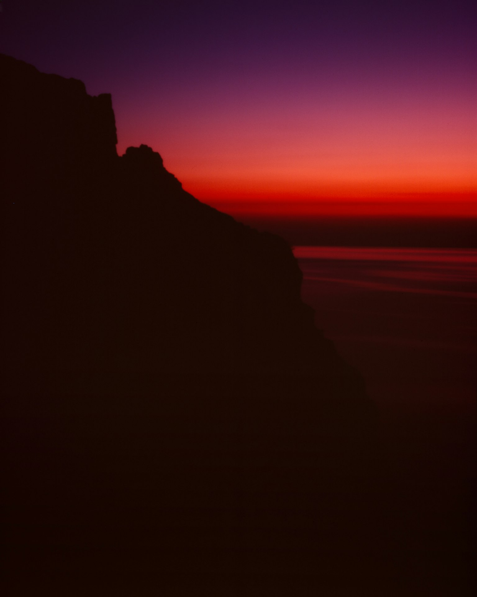 Silhouette d'une côte contre un ciel violet et un coucher de soleil orange