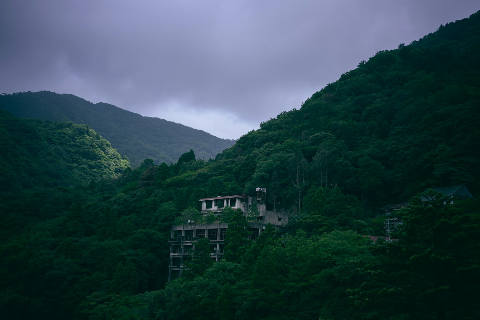 Edificio abandonado en montañas verdes bajo nubes oscuras