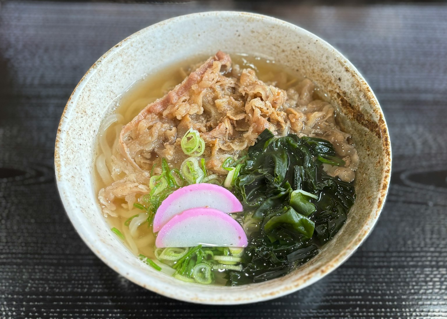 Un bol de ramen avec de la viande, des oignons verts, des algues et du gâteau de poisson tranché