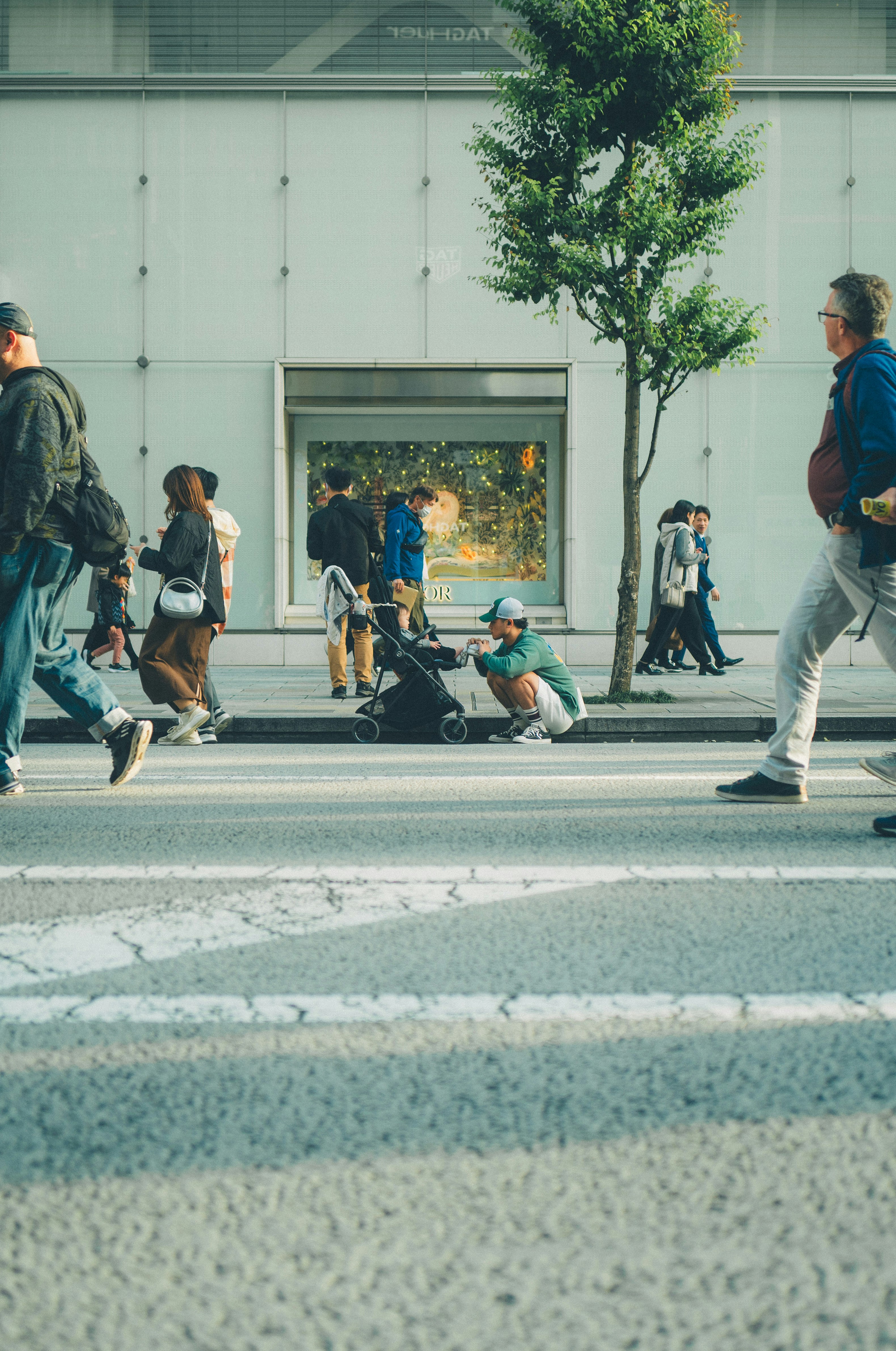 街路樹のある歩道を行き交う人々とベビーカー