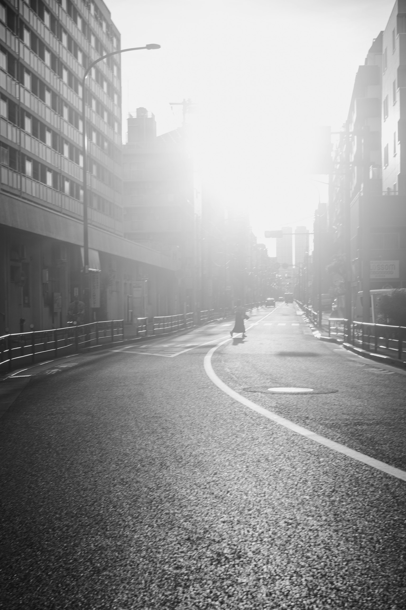 Black and white city road scene with morning sunlight shining A winding road with a vehicle and tall buildings in view