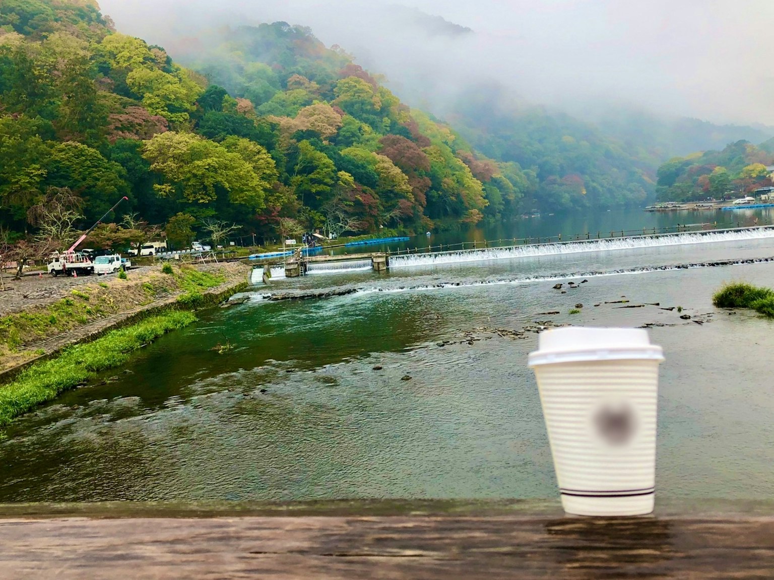 Malersicher Blick auf einen Fluss und Berge mit einem Kaffeebecher im Vordergrund