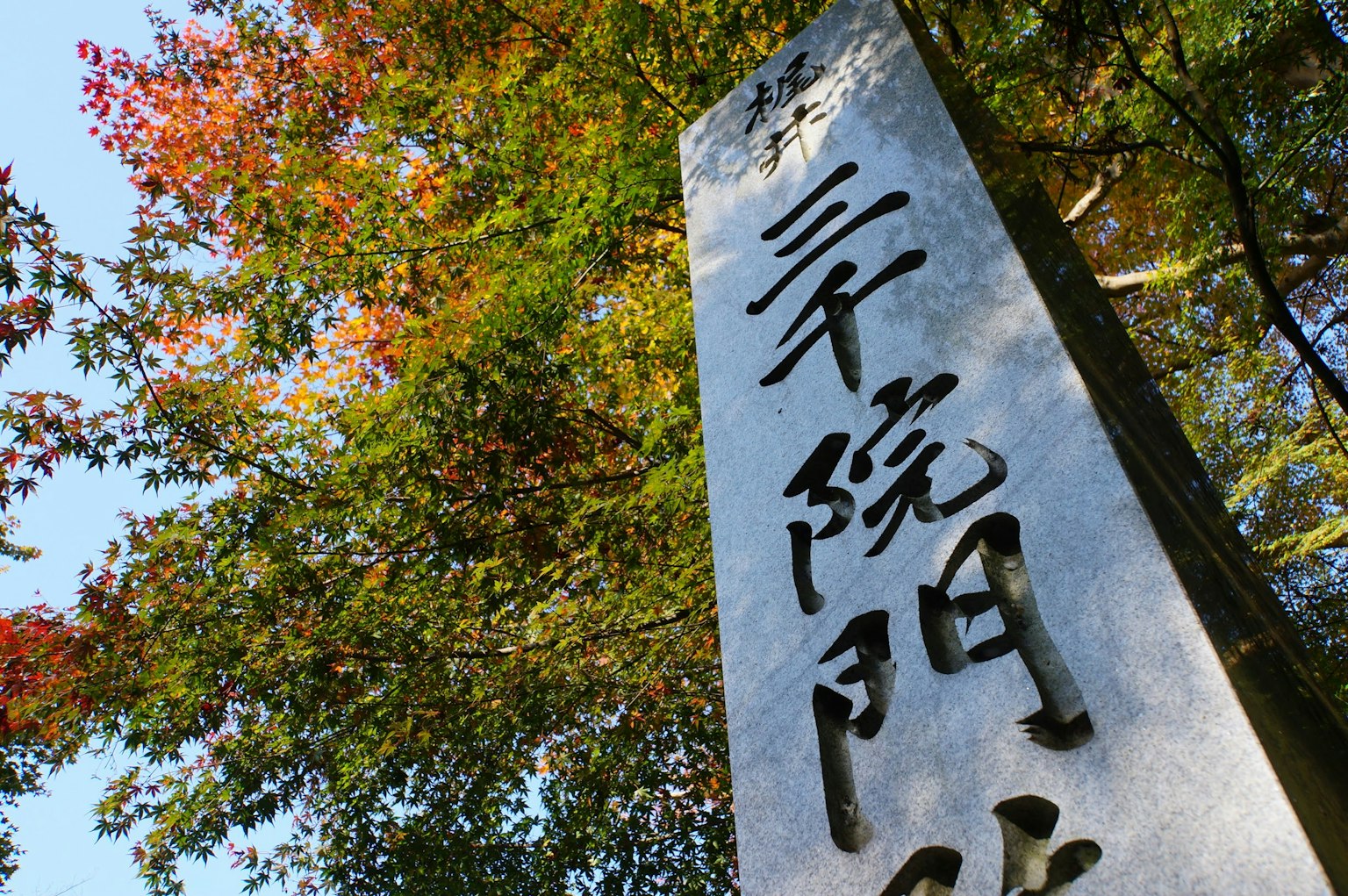 Monumento de piedra con caracteres japoneses y follaje otoñal circundante