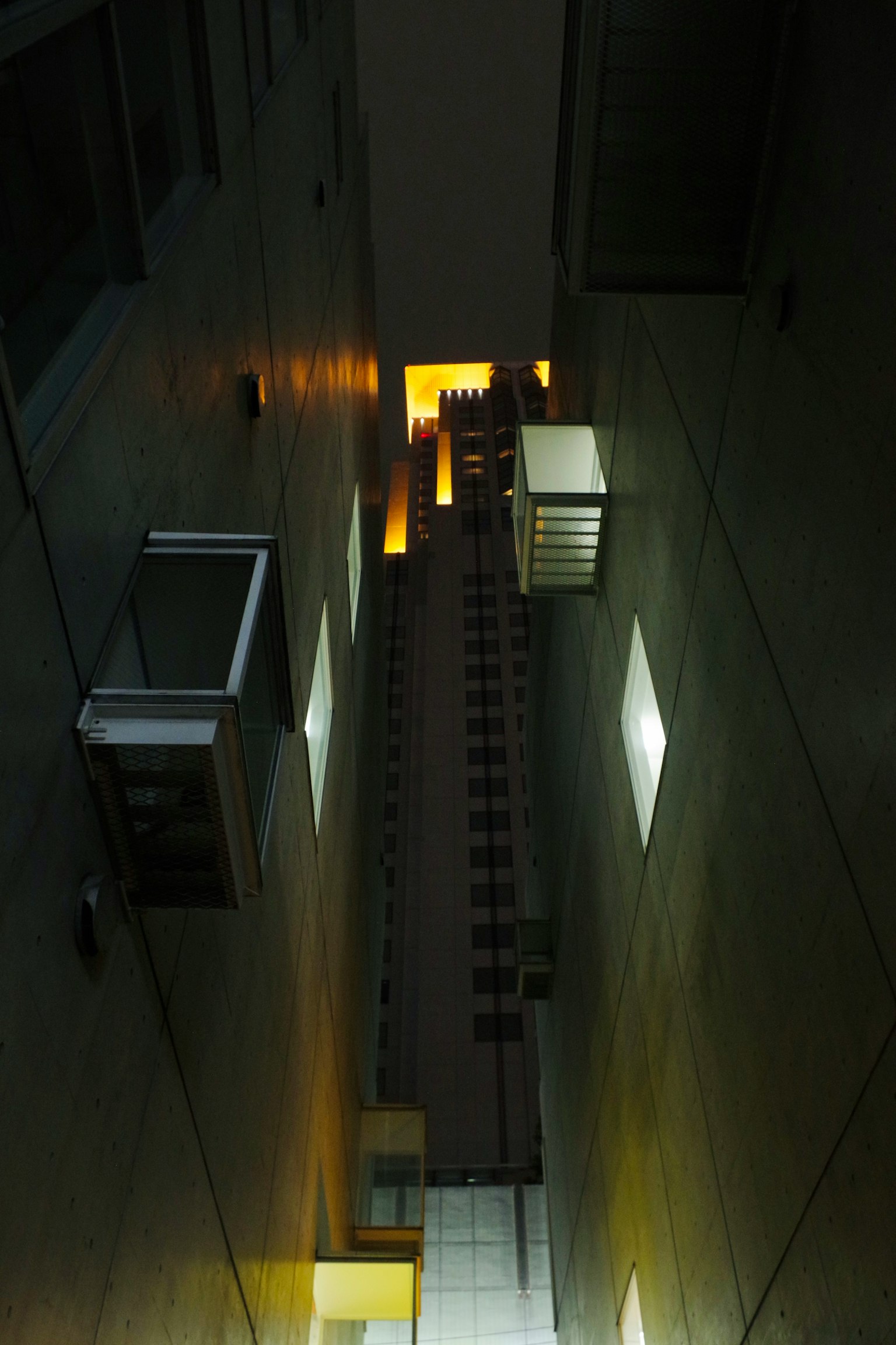 Eine Ansicht, die nachts in eine enge Gasse zwischen hohen Gebäuden nach oben schaut Helle Lichter aus Fenstern und Betonwänden sind auffällig