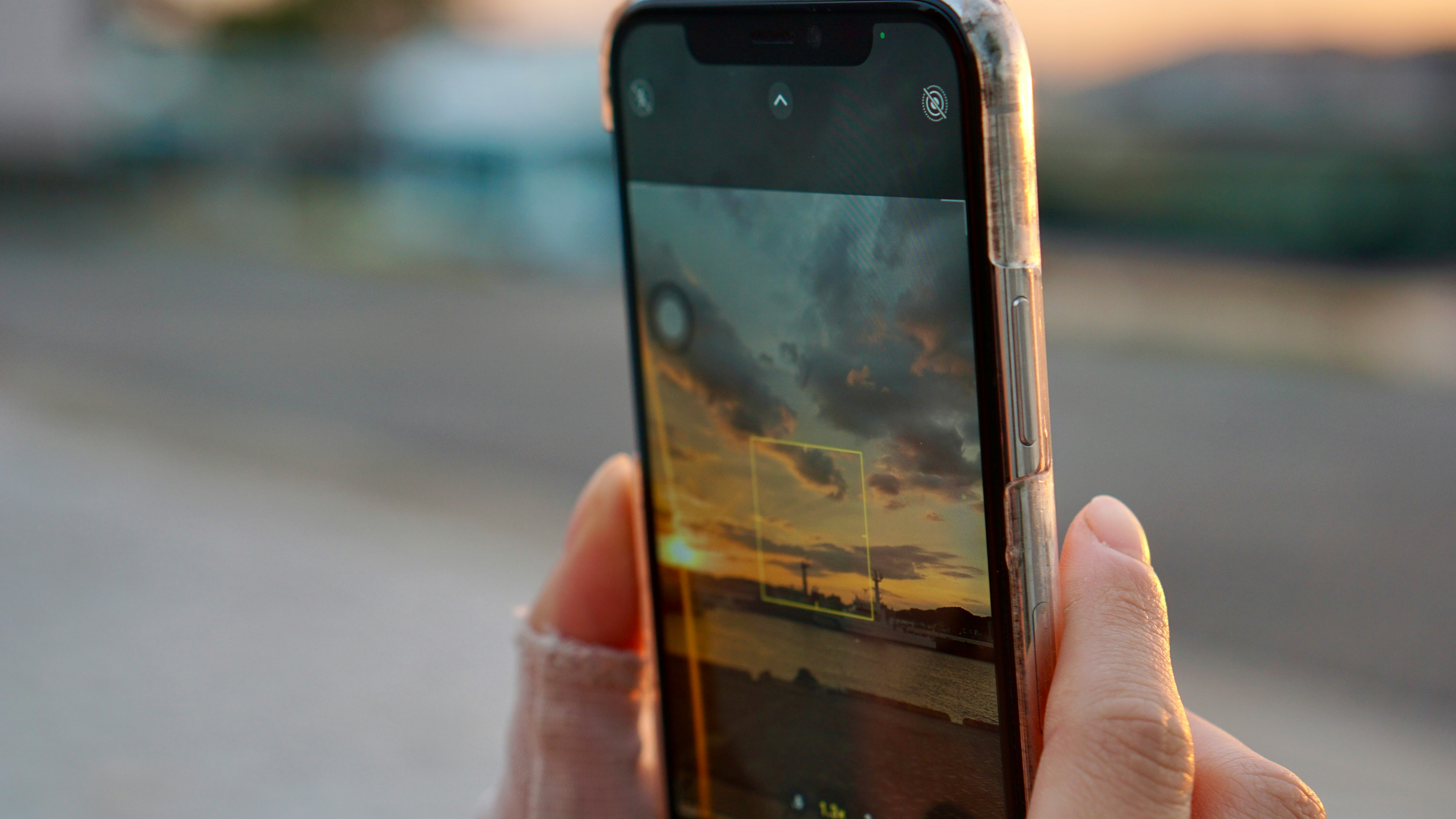 Hand hält ein Smartphone mit einer Sunset-Landschaft auf dem Display