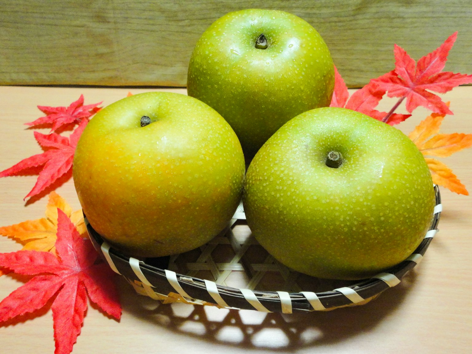Tres manzanas verdes en una cesta rodeadas de hojas de otoño