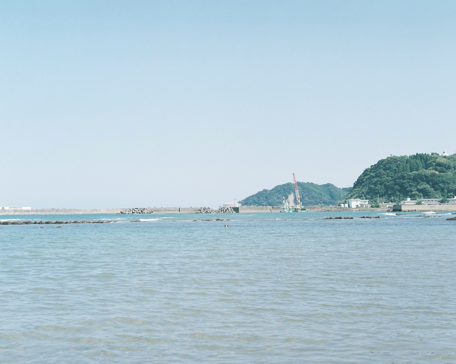 푸른 바다와 부드러운 파도, 멀리 보이는 산과 구조물