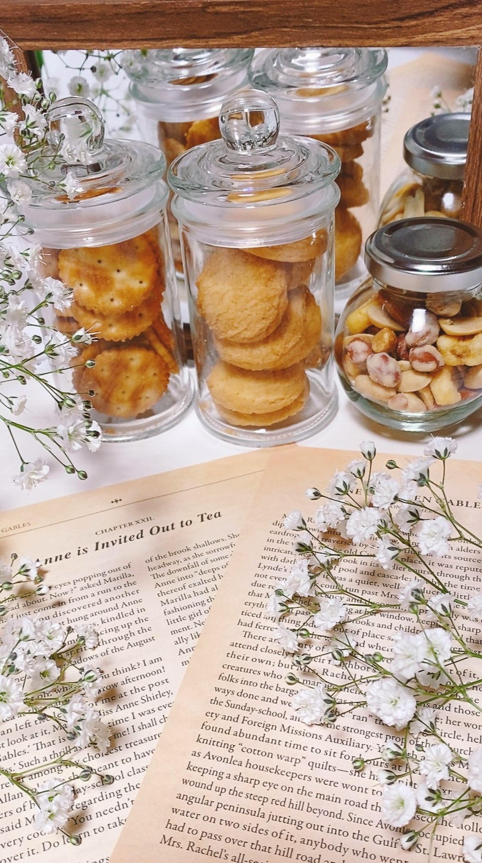 Meja dengan buku terbuka dikelilingi toples kaca berisi kue dan dihiasi bunga
