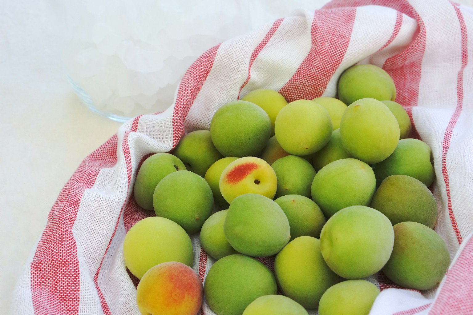 Un panier de prunes vertes avec une touche de rouge sur un tissu rayé rouge et blanc