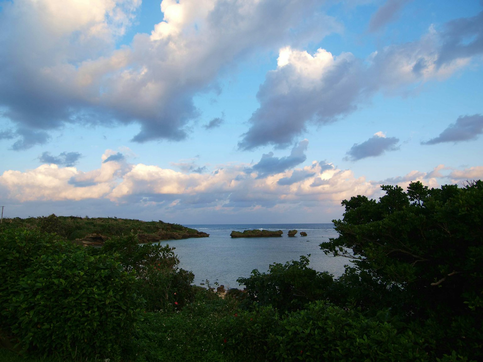 Scenic view of the sea under a blue sky with white clouds Green trees in the foreground small islands in the distance
