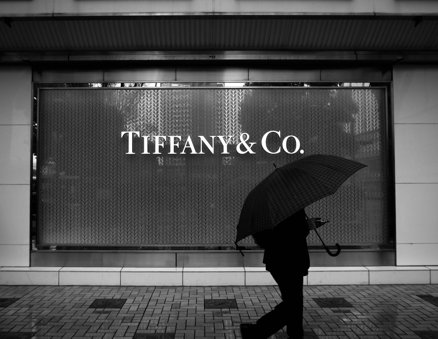 Silhouette einer Person, die mit einem Regenschirm vor einem Tiffany & Co. Geschäft geht