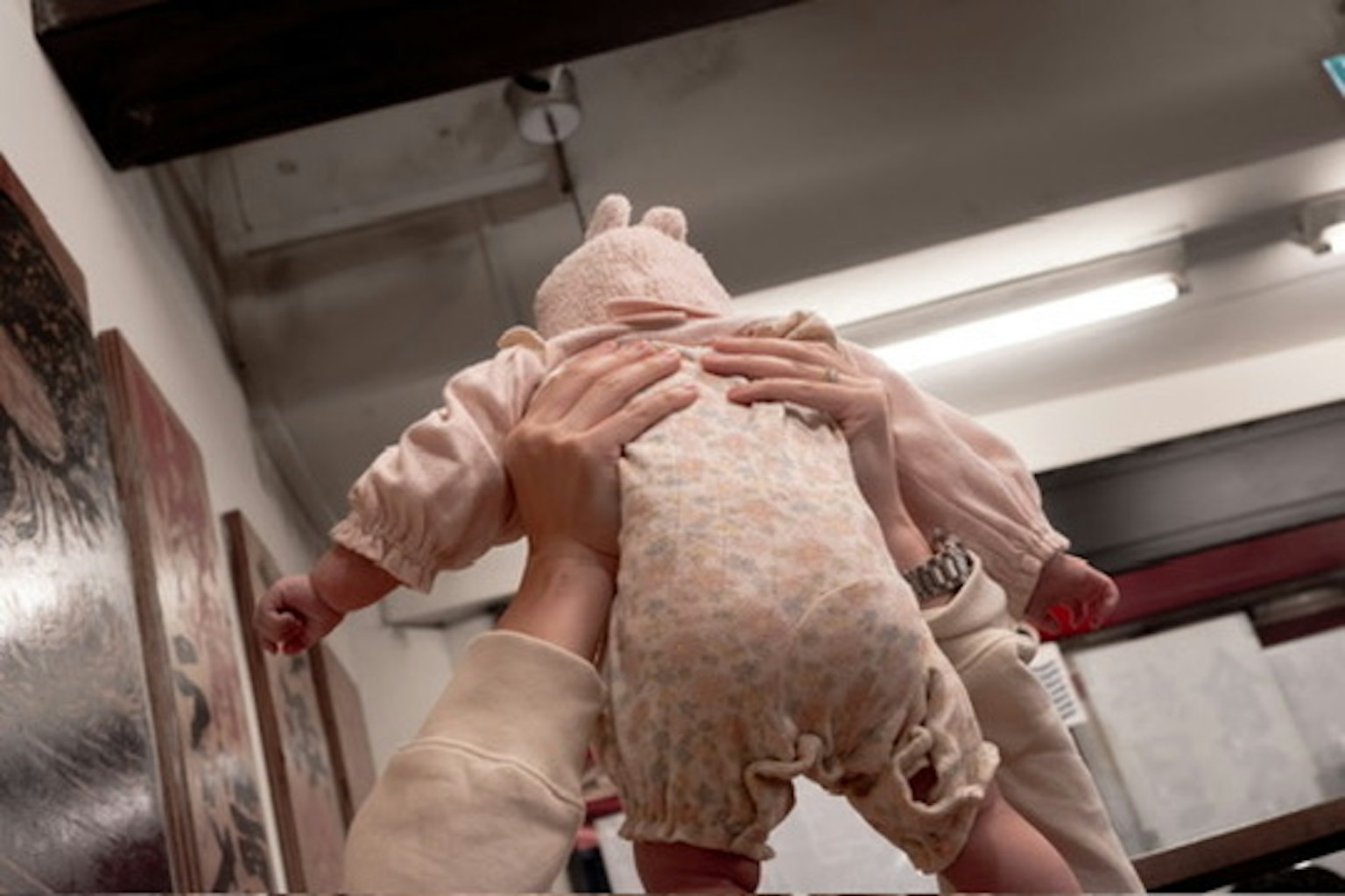 Una persona che solleva un bambino con un vestito chiaro su uno sfondo di muro bianco