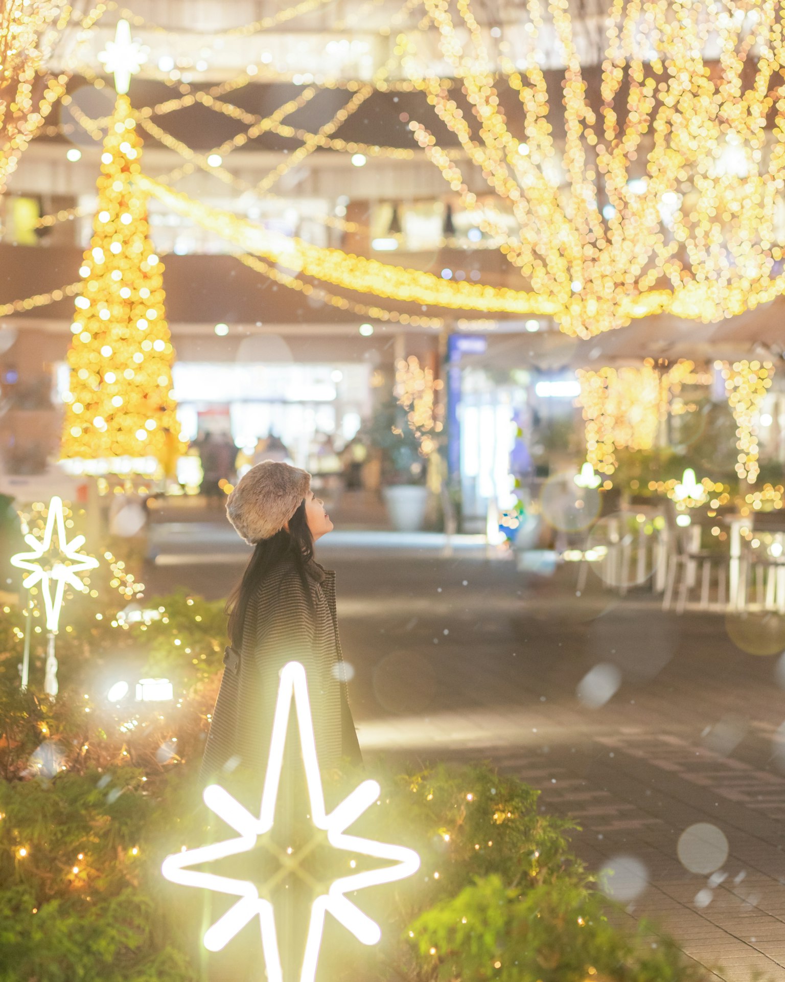 Person standing in a street adorned with Christmas lights