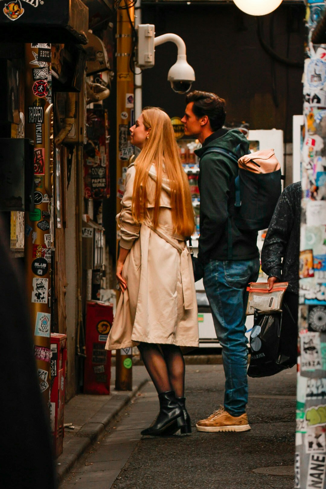 Ein Paar schaut in einer engen Gasse mit bunten Plakaten um sich herum nach oben