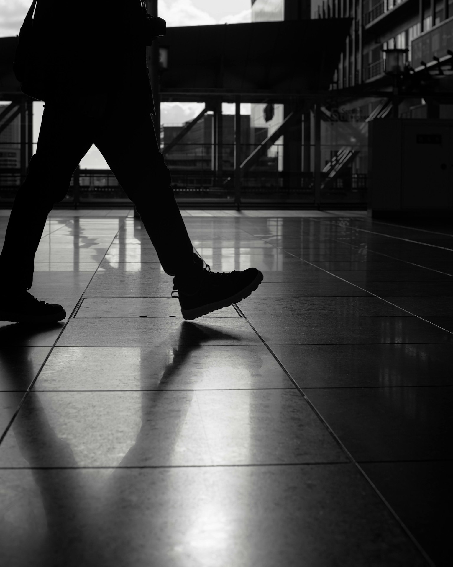 Silhouette di una persona che cammina su un pavimento lucido con scarpe nere