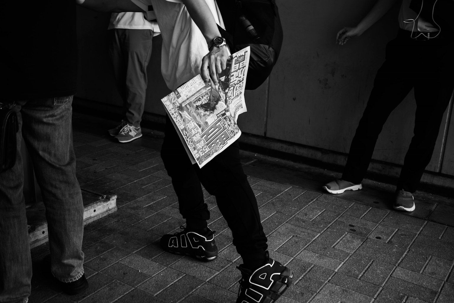 Schwarzweißfoto einer Person, die eine Zeitung hält, umgeben von anderen Personen