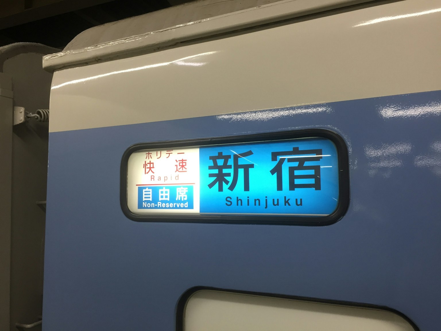 Segnale del treno per Shinjuku con sfondo blu e lettere bianche