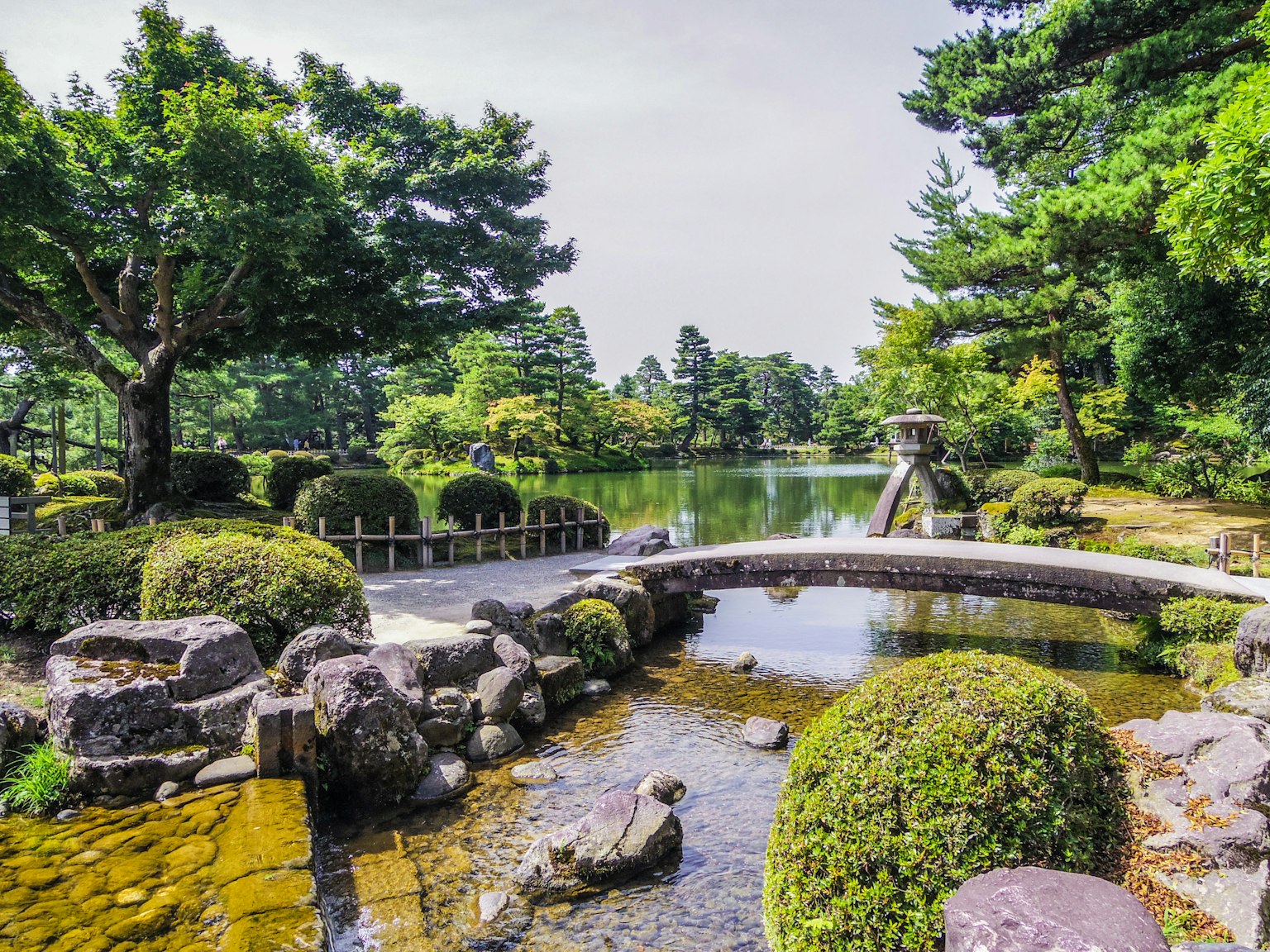 Hermoso jardín japonés con un puente y un estanque rodeado de árboles verdes y esculturas de piedra