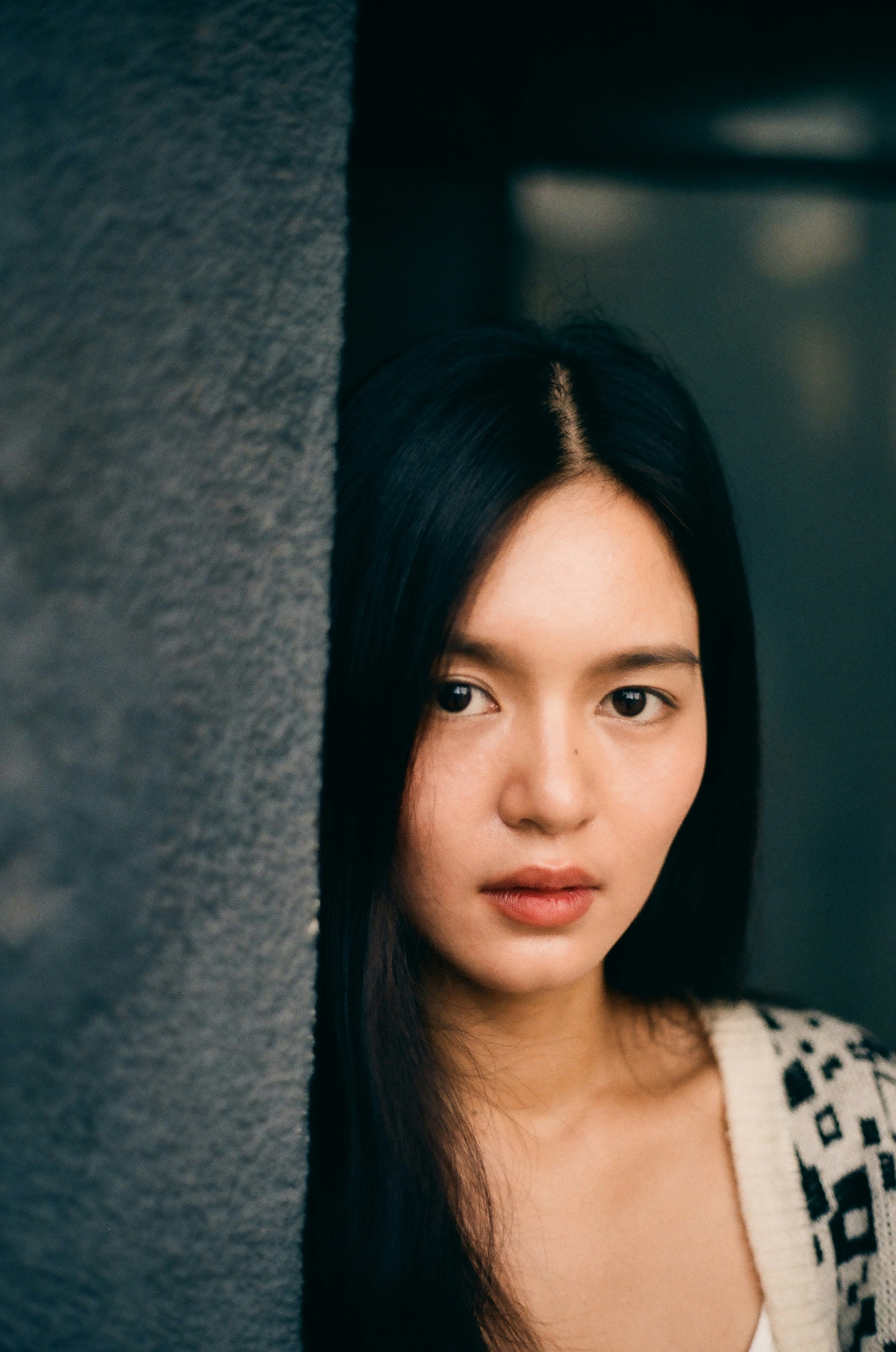 壁際に立つ黒髪の女性のポートレート