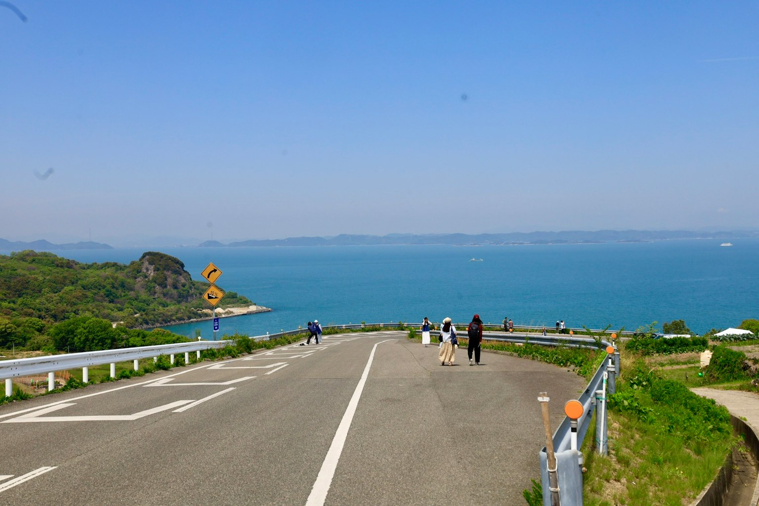 Vista panoramica di una strada che porta a un mare blu con colline verdi Persone che camminano lungo il sentiero