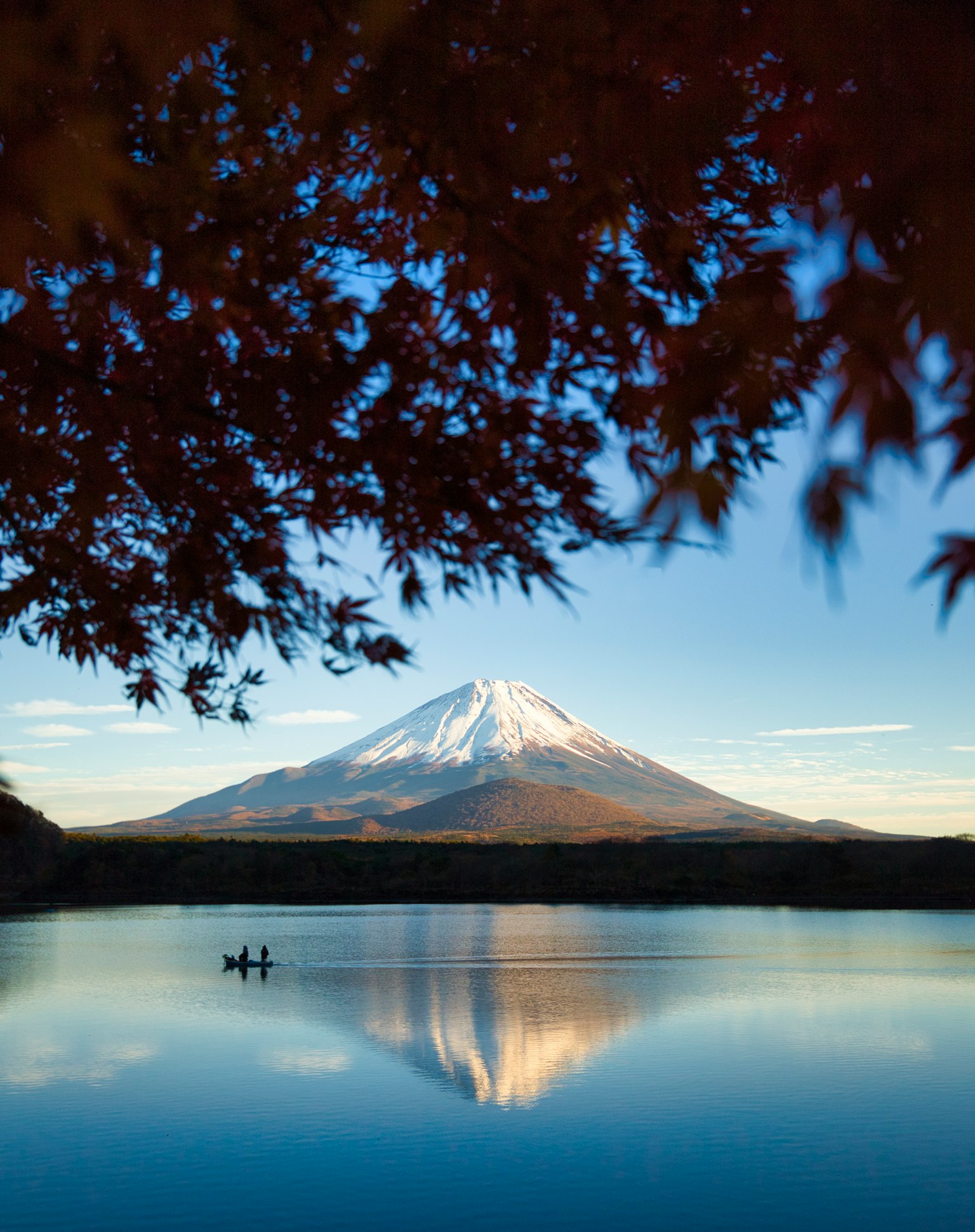 Vista panoramica del monte Fuji riflesso in un lago calmo incorniciato da foglie autunnali