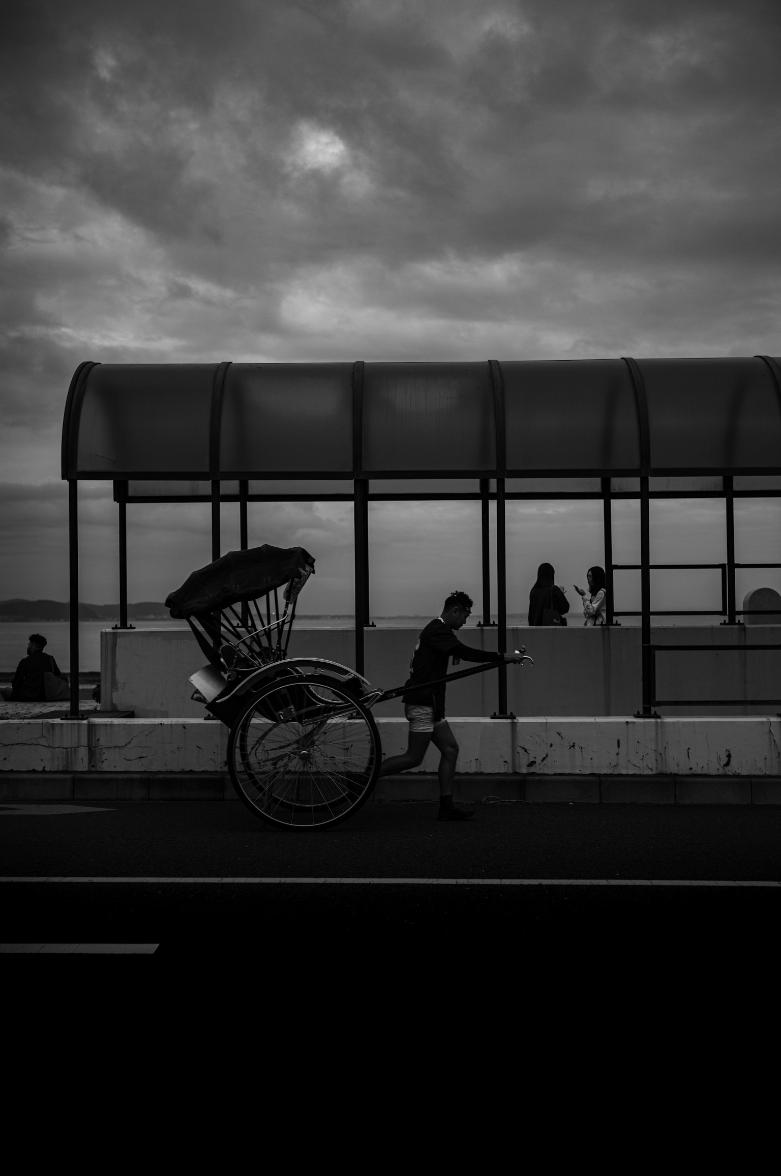 Foto in bianco e nero di una persona che tira un risciò a una fermata dell'autobus