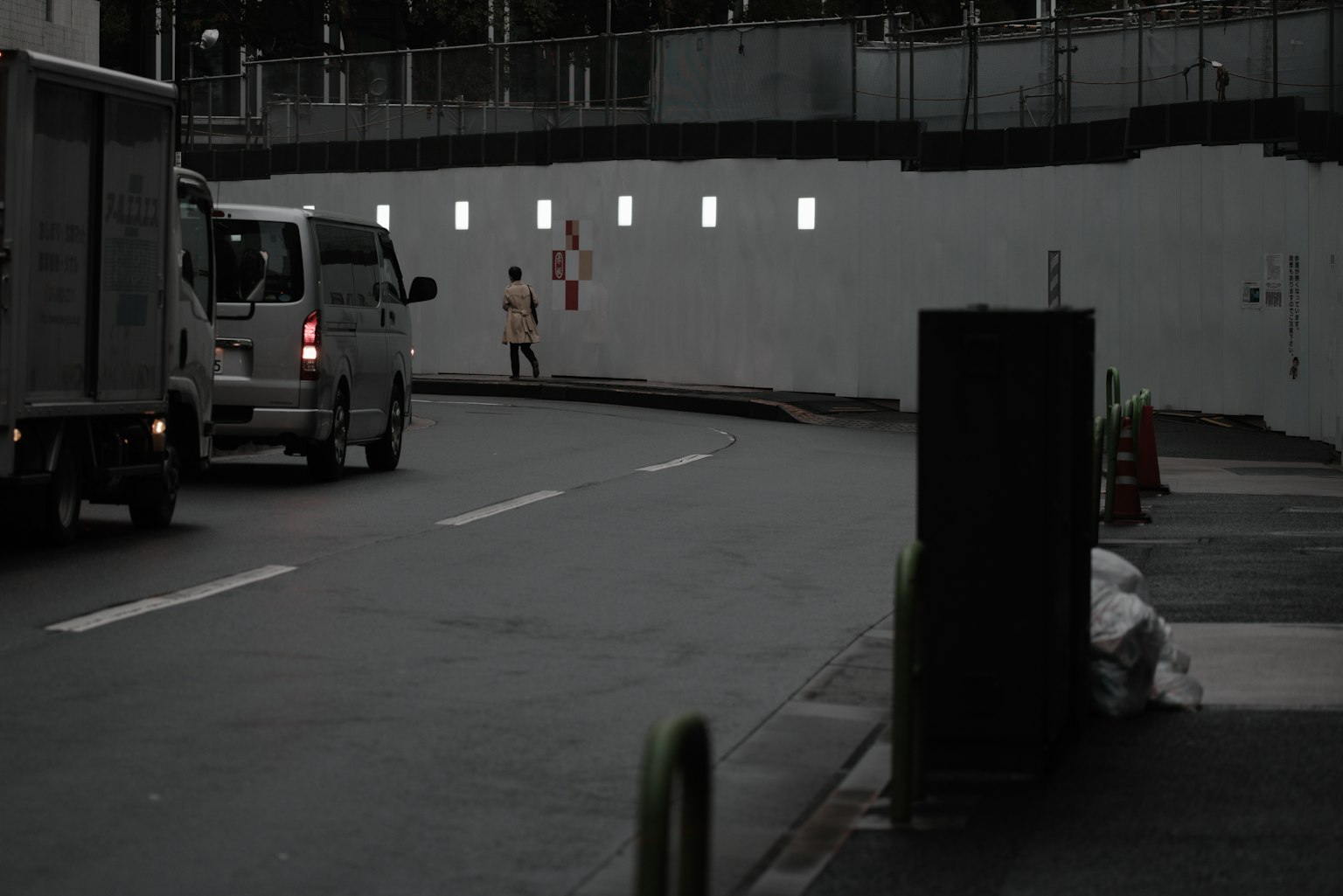 車輛沿著昏暗街道行駛，白牆上有小窗戶