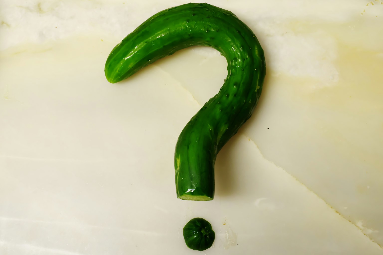 Opera d'arte a forma di punto interrogativo realizzata con un cetriolo verde