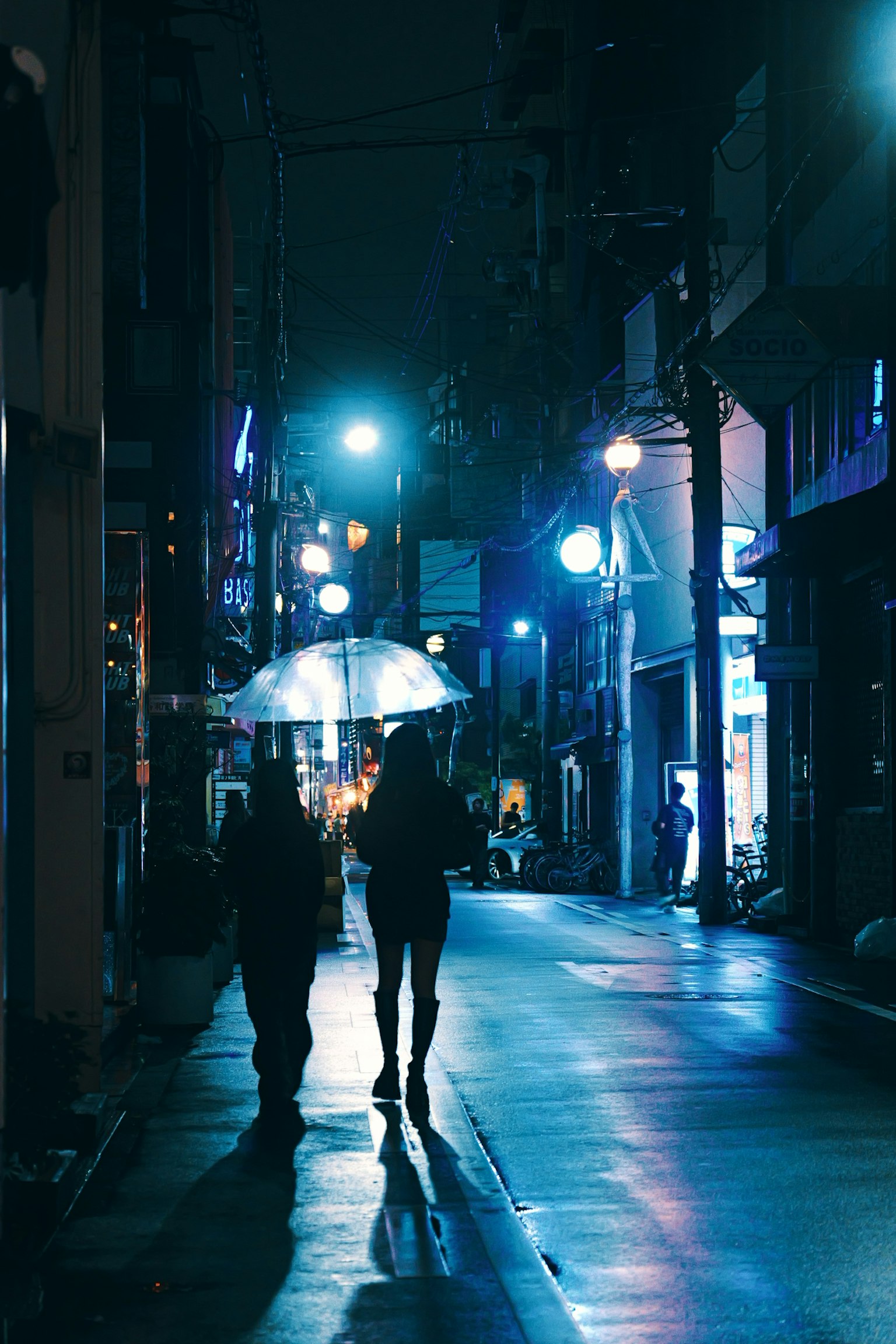 夜の街を歩く二人のシルエットと傘の光