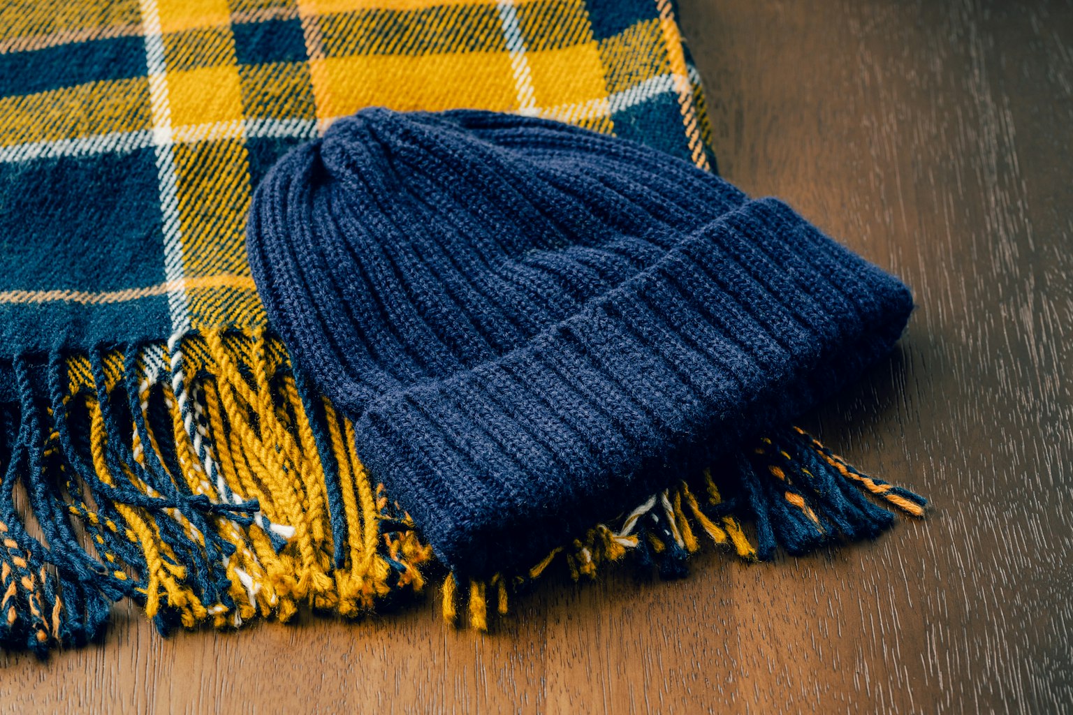 Navy gestrickte Mütze und gelb-blau karierter Schal auf einem Holztisch