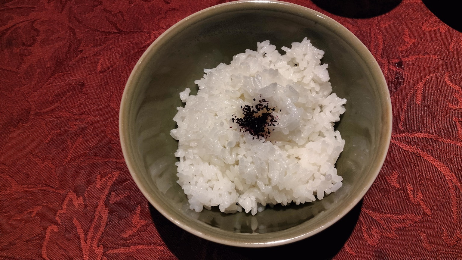 红色桌子上中央有深色酱汁的白米饭碗