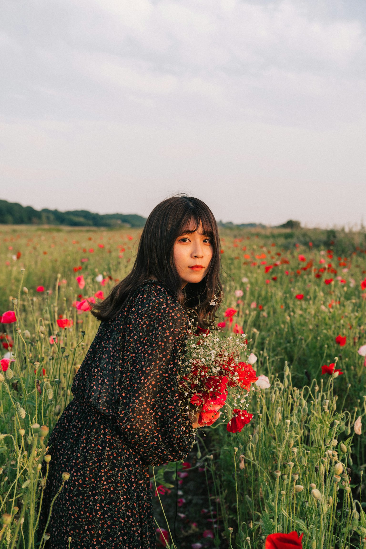 꽃다발을 들고 꽃밭에 서 있는 여성