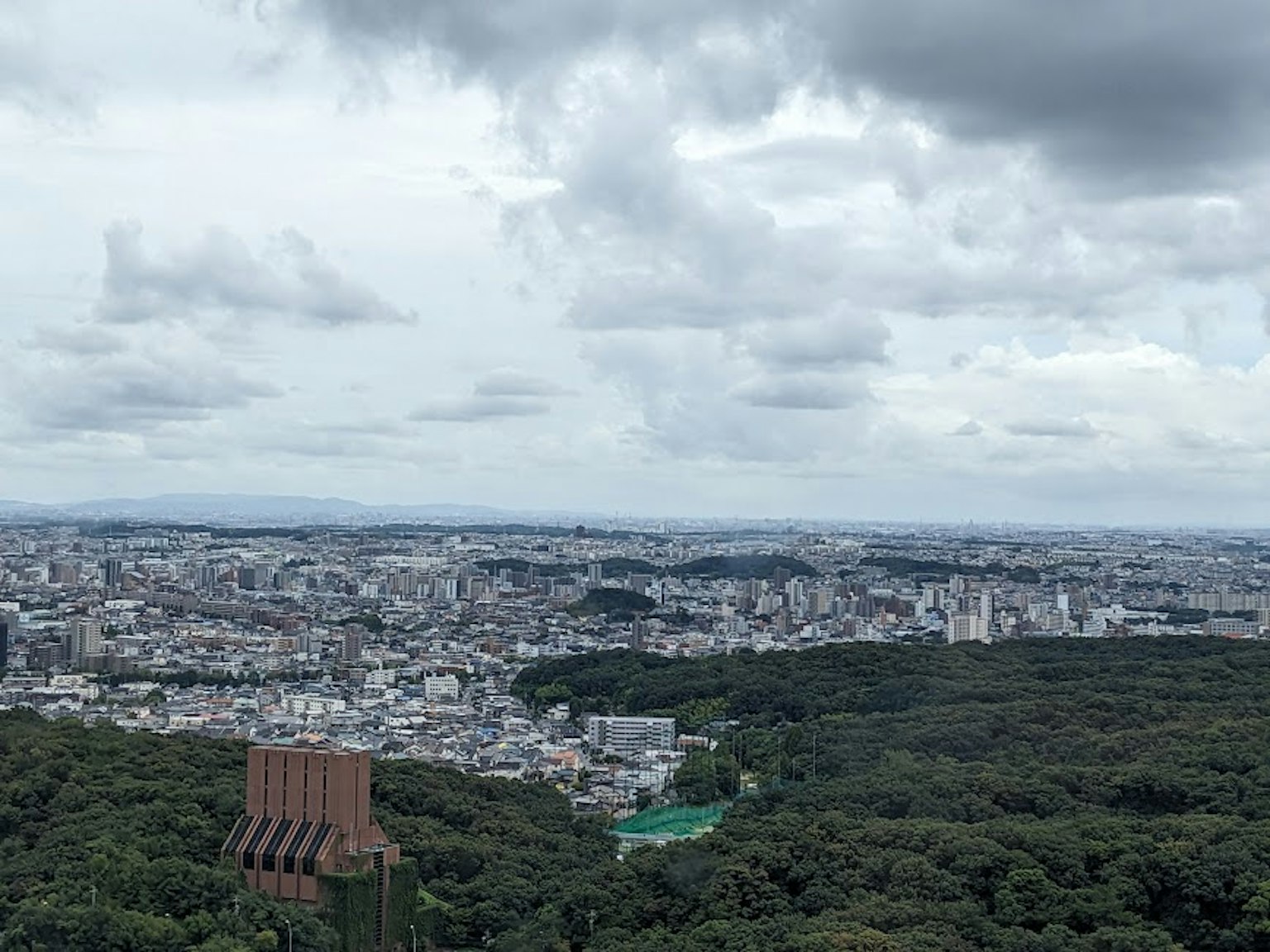 綠色山丘上的城市全景在多雲的天空下展示建築和住宅區