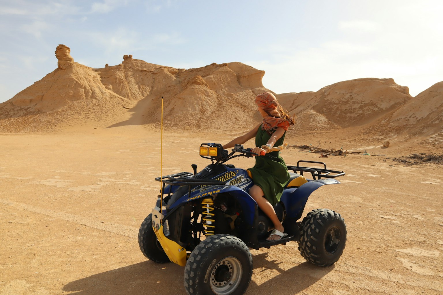Mujer montando un ATV en un paisaje desértico con dunas de arena