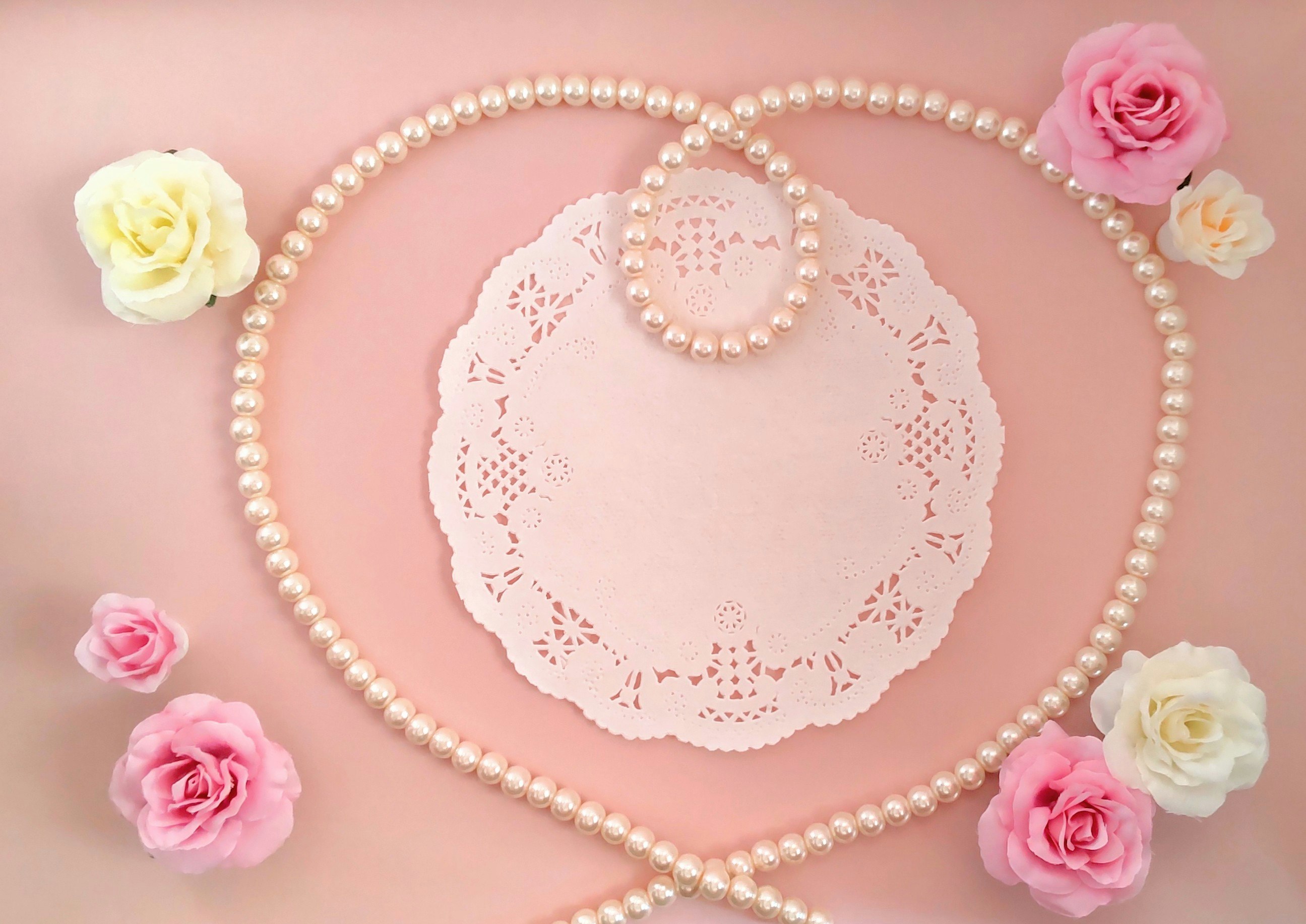 Pearl necklace and lace paper flower decorations on a pink background