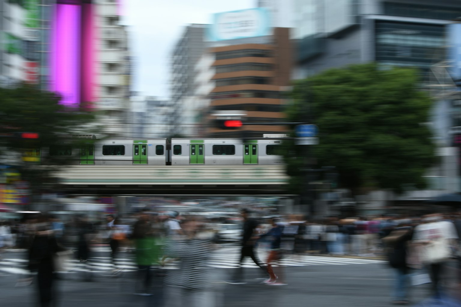 模糊的城市交叉口，行人穿越，綠色火車在上方