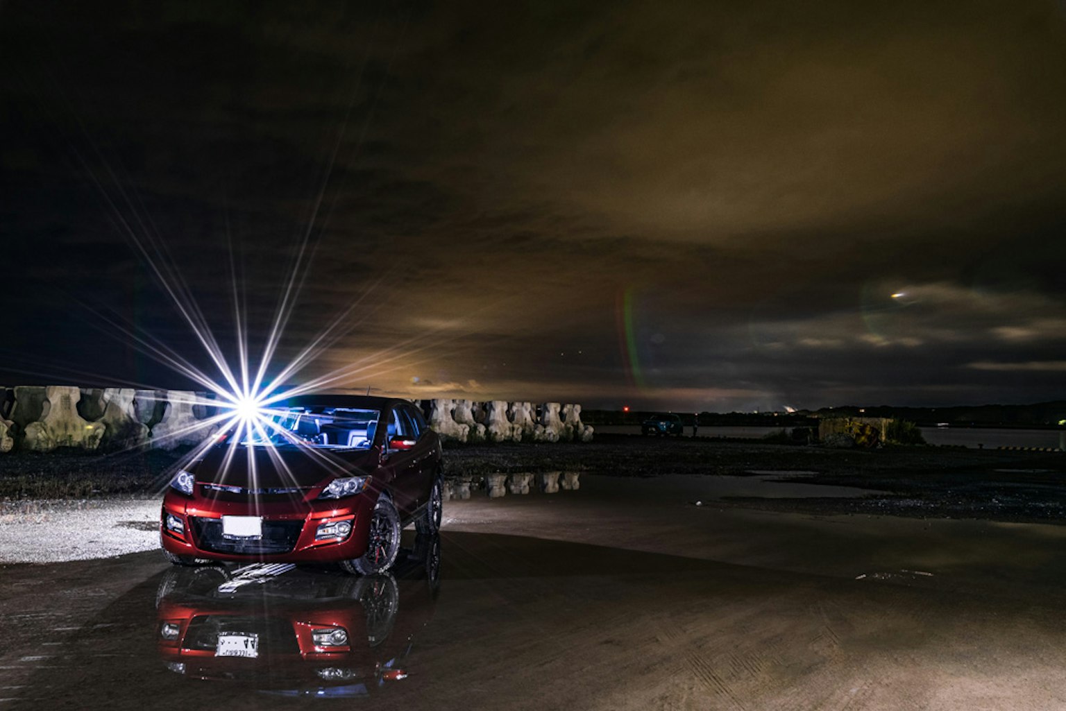 Rotes Auto unter dunklem Himmel mit leuchtenden Scheinwerfern