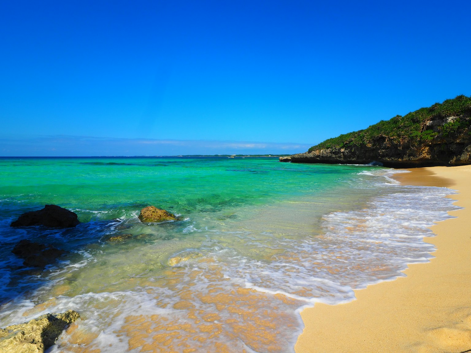 ทิวทัศน์ชายหาดที่มีท้องฟ้าสีฟ้าสดใสและน้ำทะเลสีเขียวมรกต