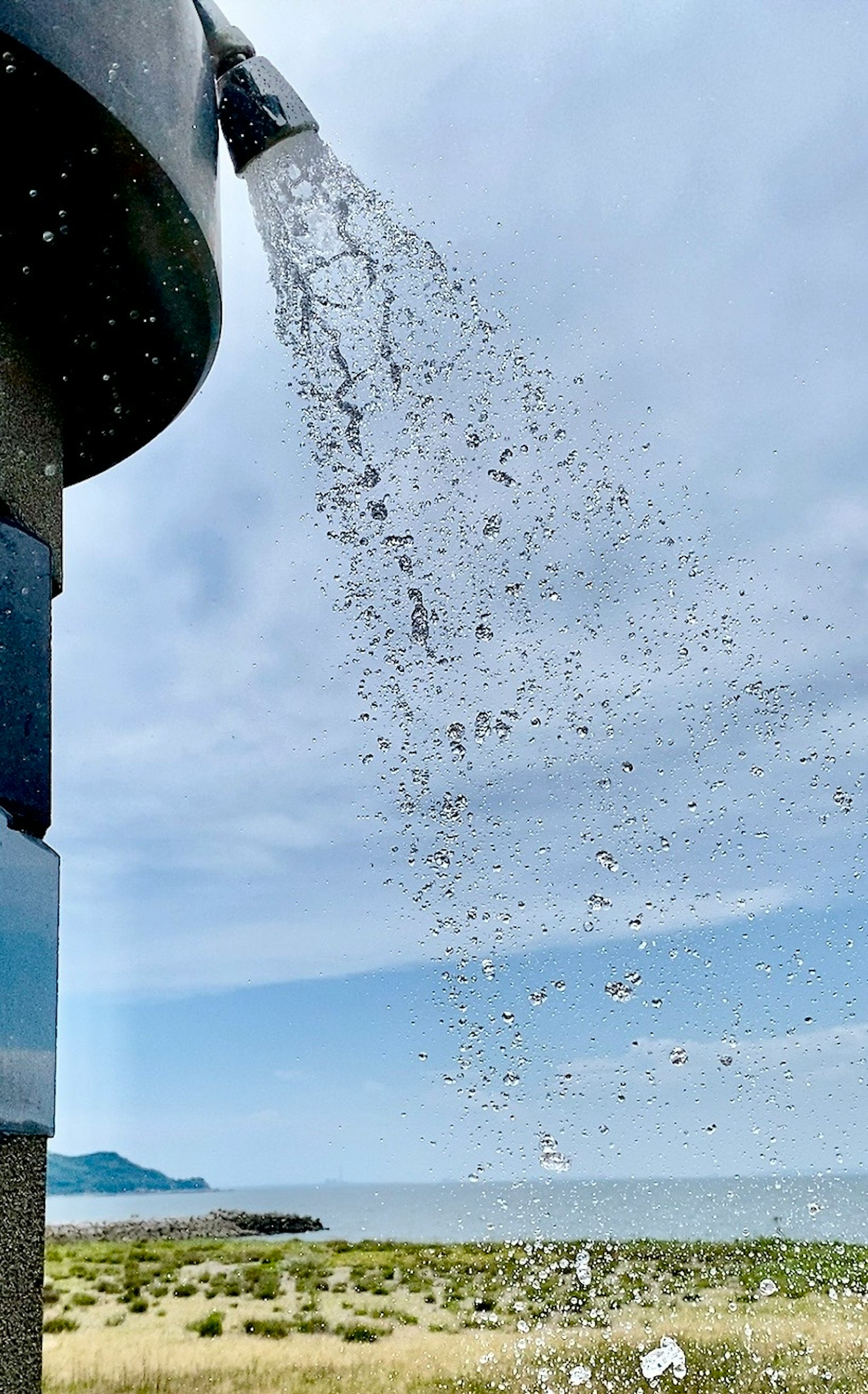 Agua fluyendo de una tubería con vista al cielo azul y al mar