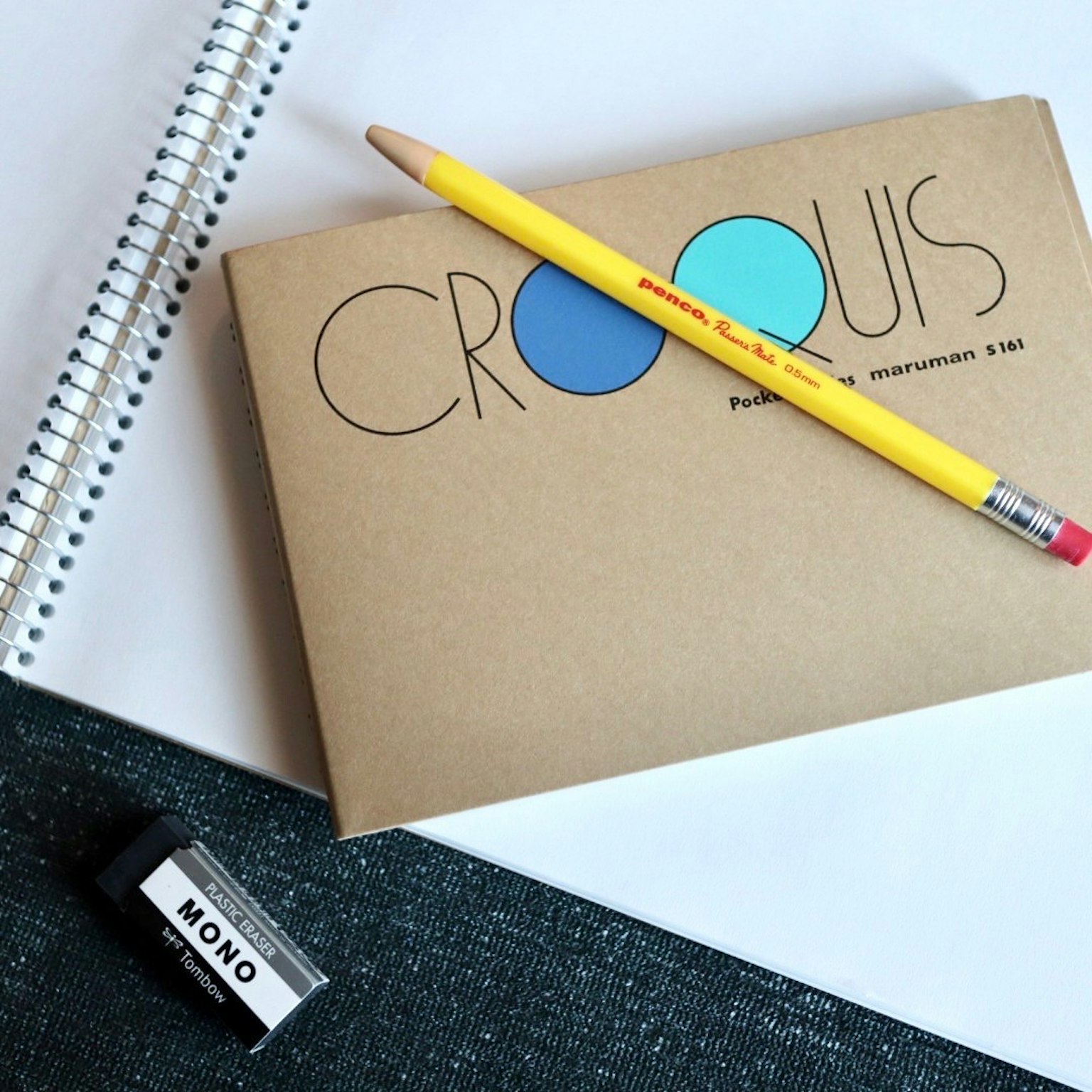 Cuaderno de bocetos CROQUIS con un círculo azul y un lápiz amarillo sobre un fondo de papel blanco