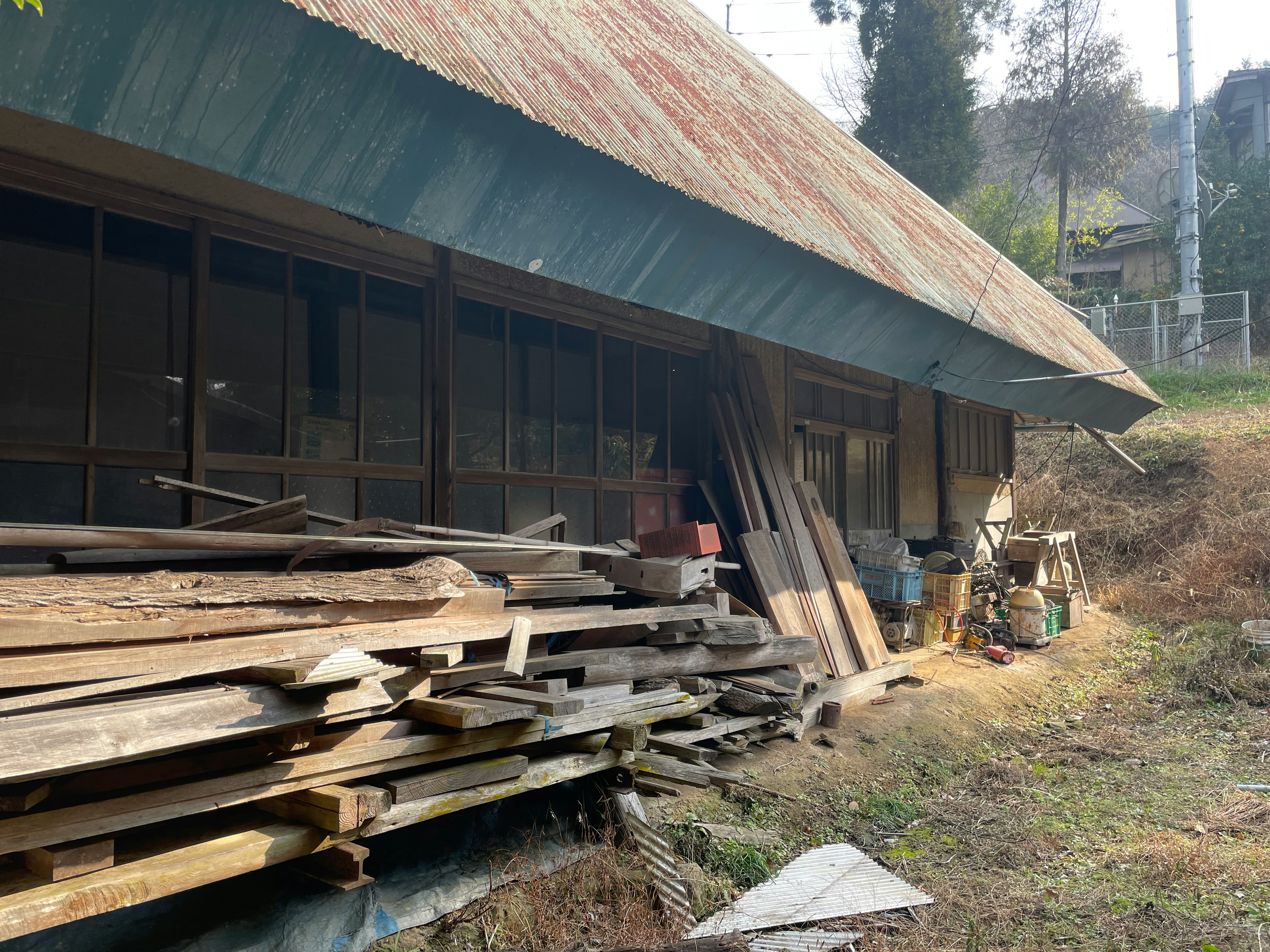 山の中の廃屋の軒先に積まれた木材と板材