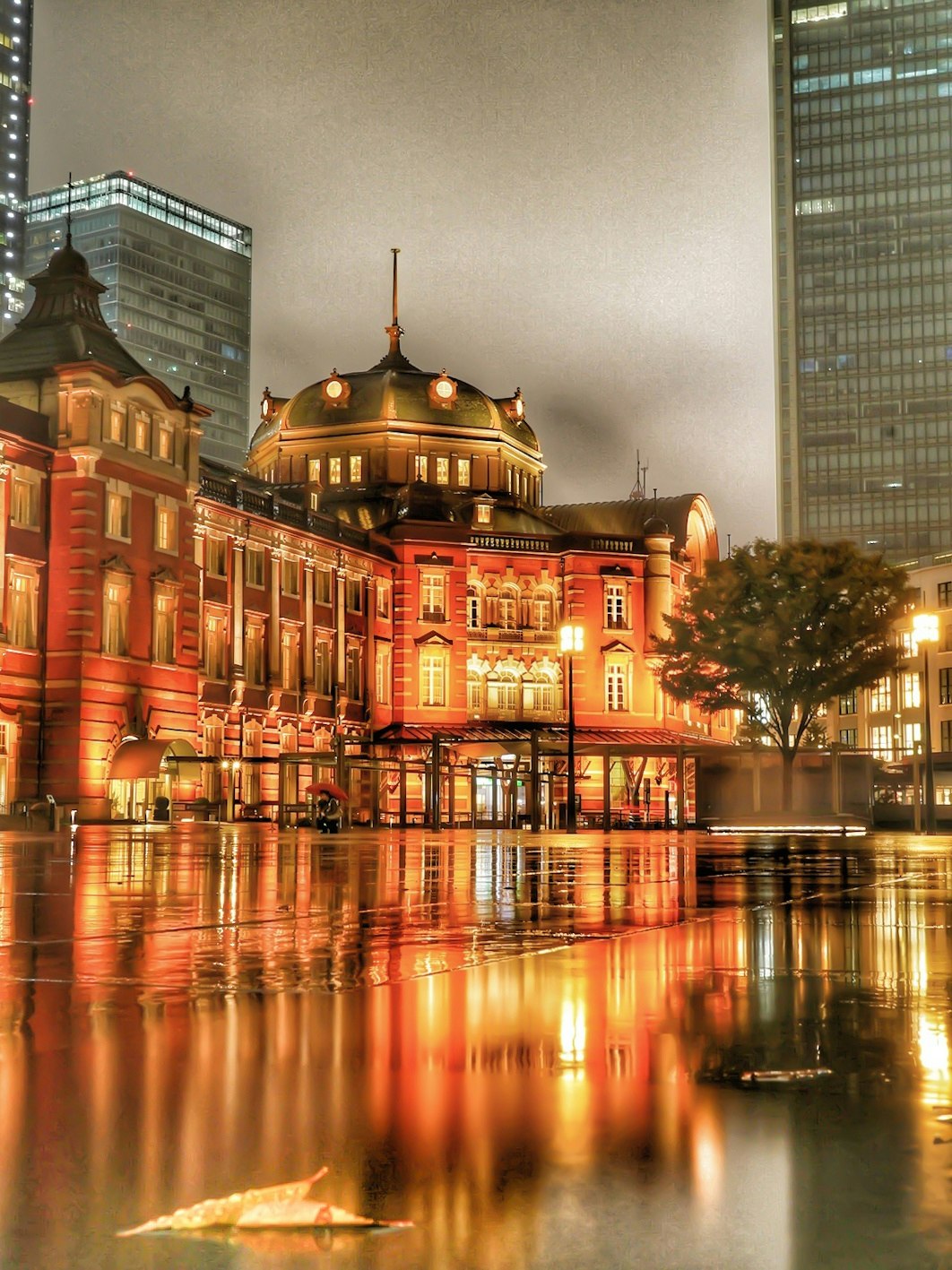 雨の東京駅前に映る夜景のドームとレンガ建築