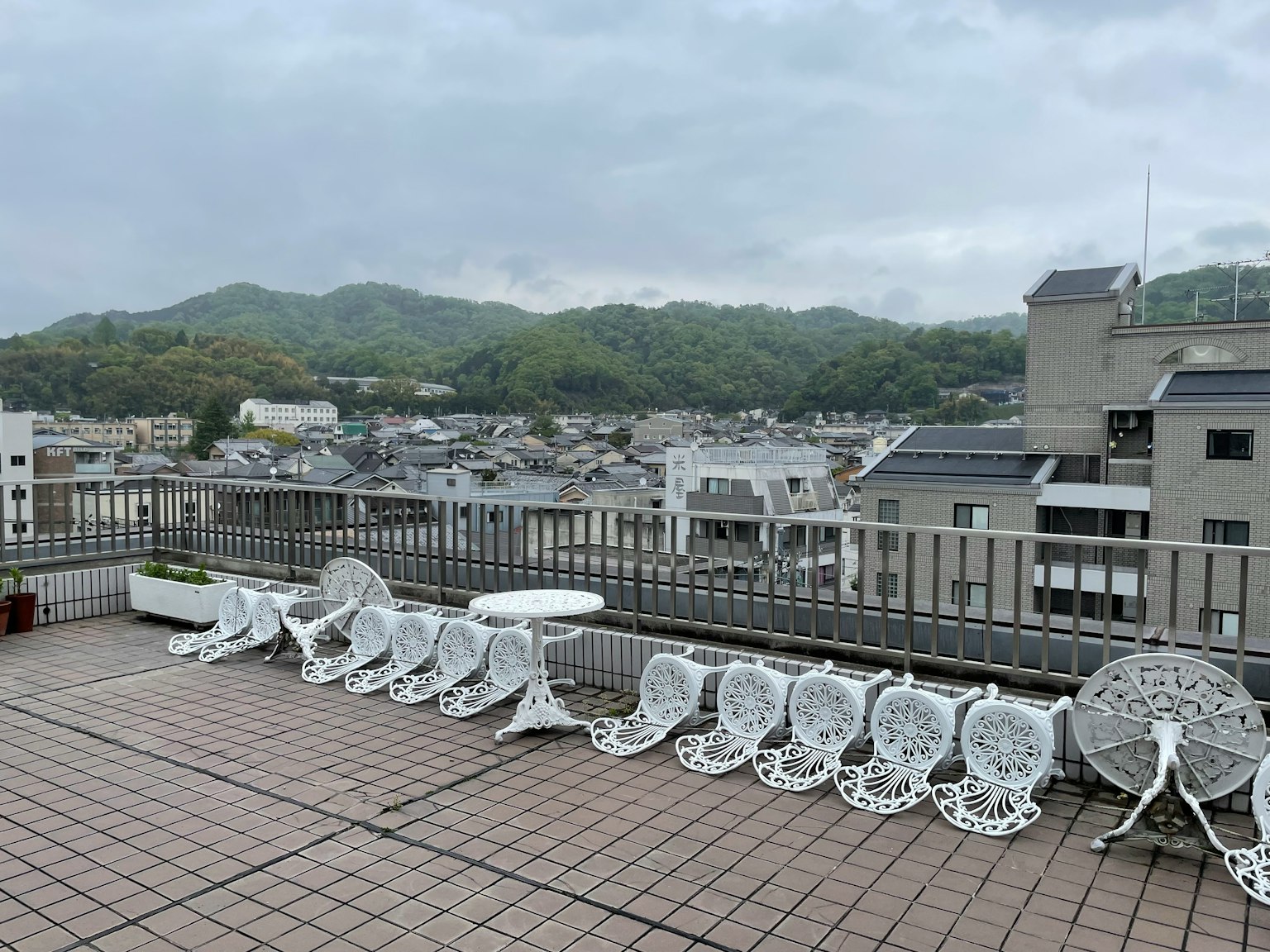 Aussicht von einem Dach mit weißen Stühlen und einem Tisch über grüne Hügel und Stadtgebäude