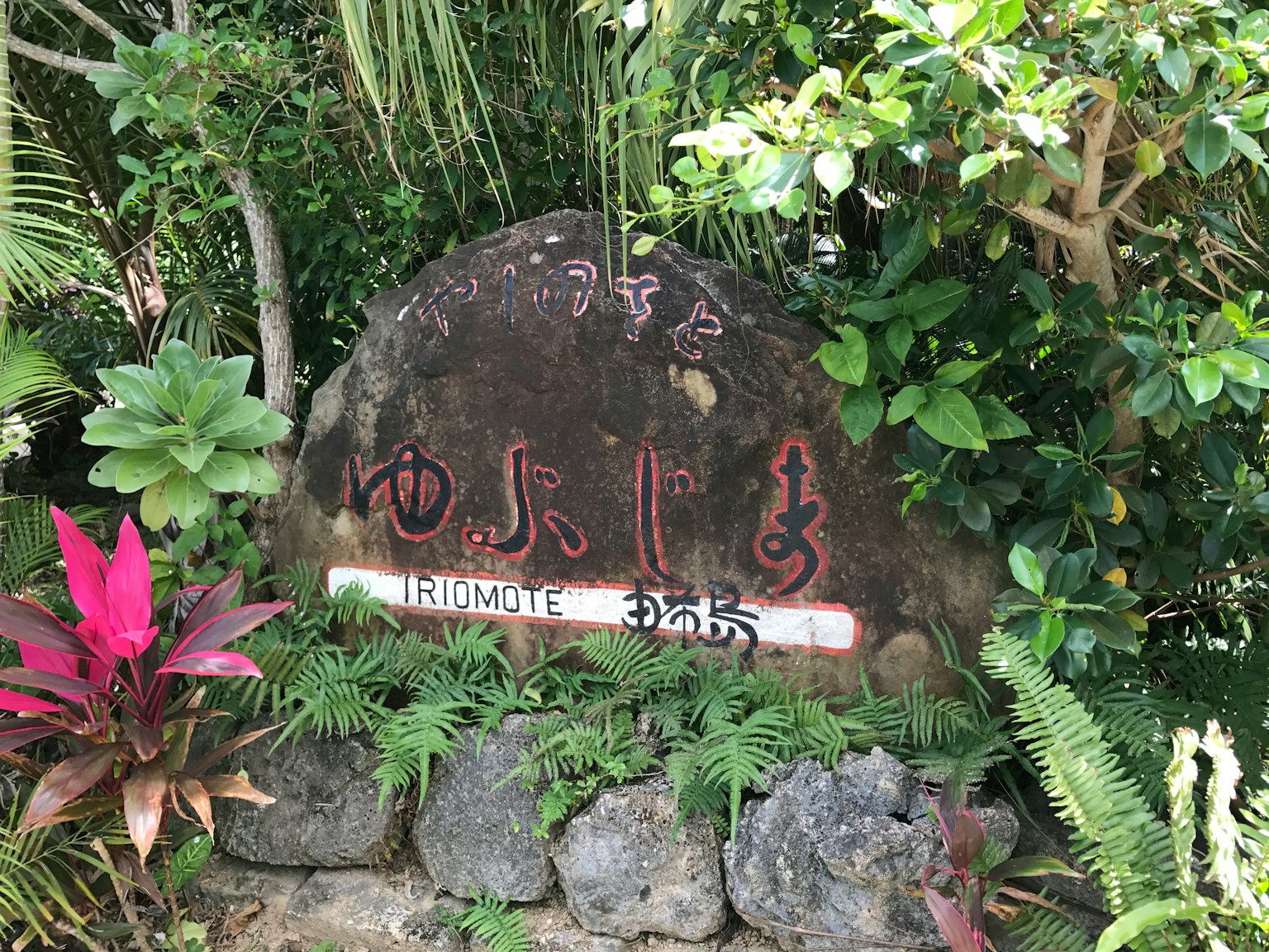 Cartel de piedra rodeado de plantas verdes exuberantes con letras rojas distintivas