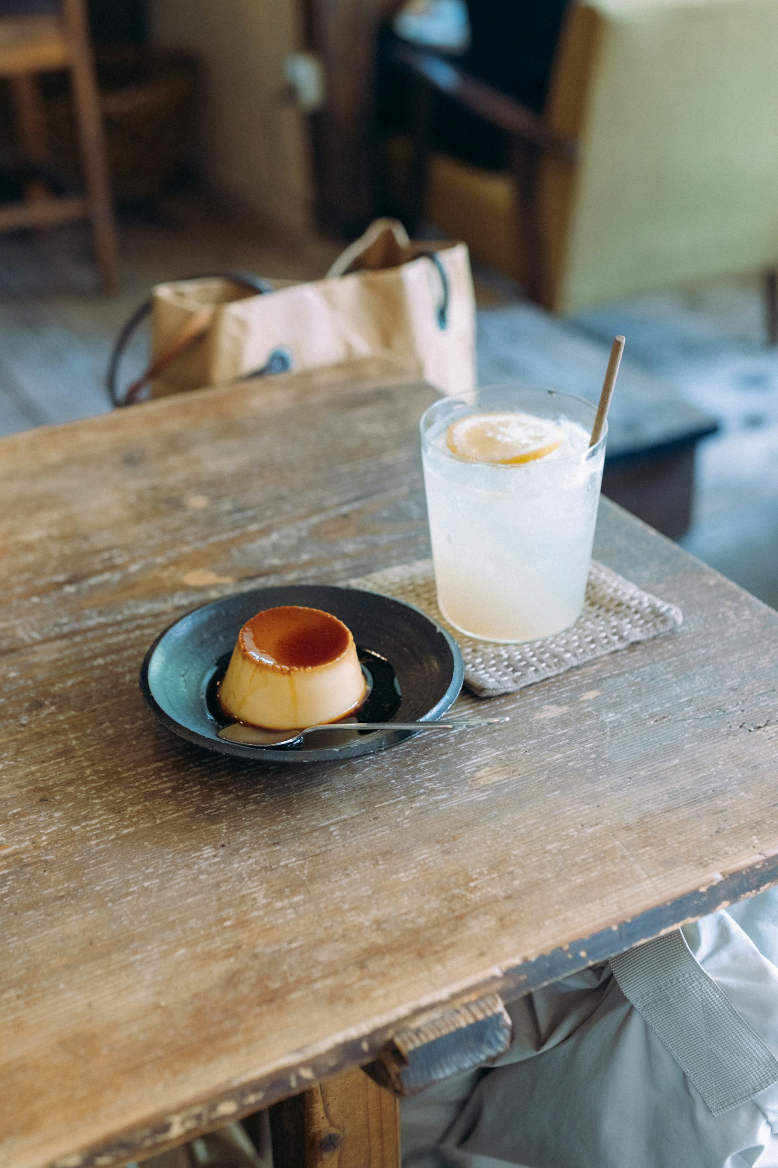Bánh flan trên đĩa đen bên cạnh một cốc đồ uống lạnh trên bàn gỗ