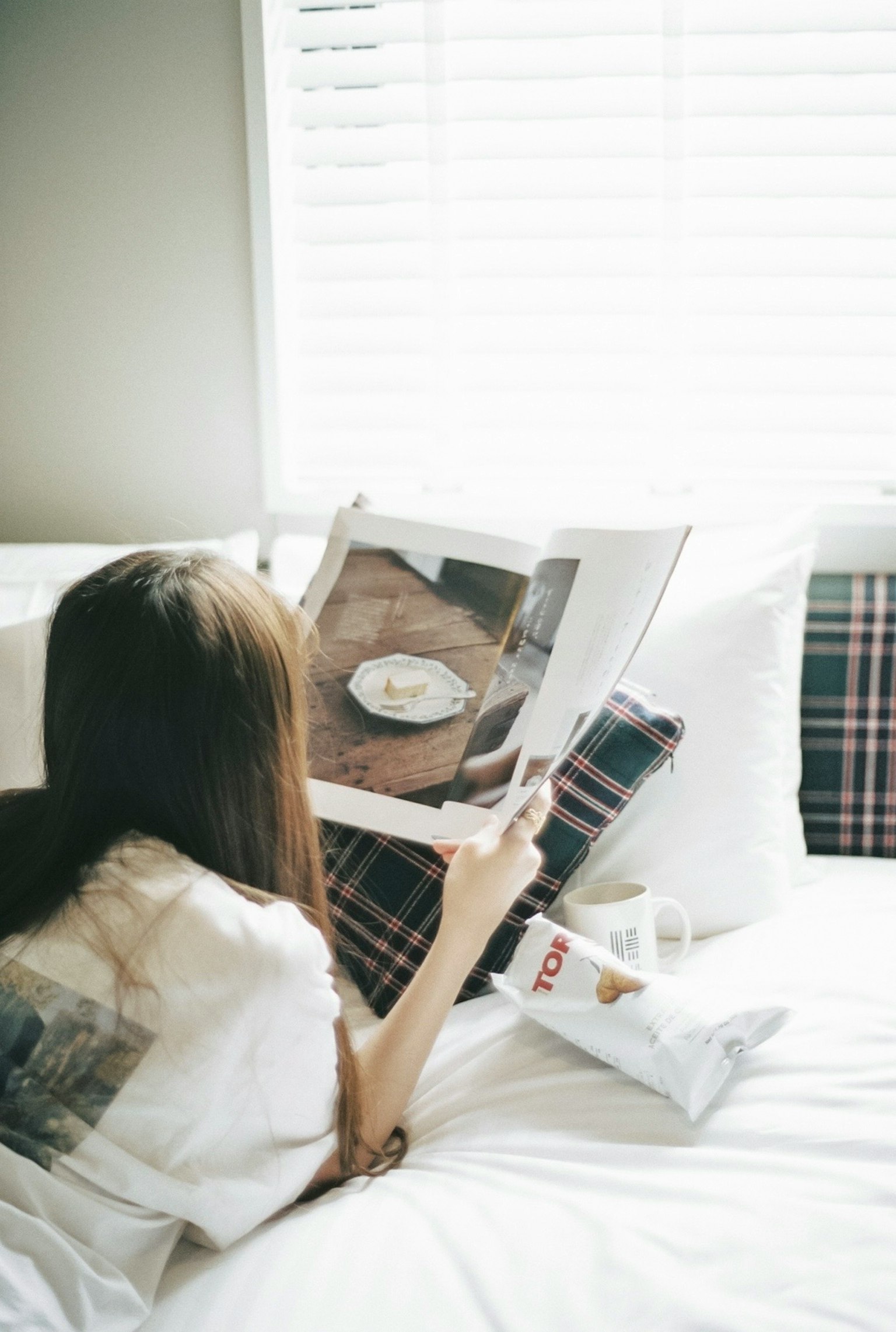 Một người phụ nữ đang đọc tạp chí trên giường có gối