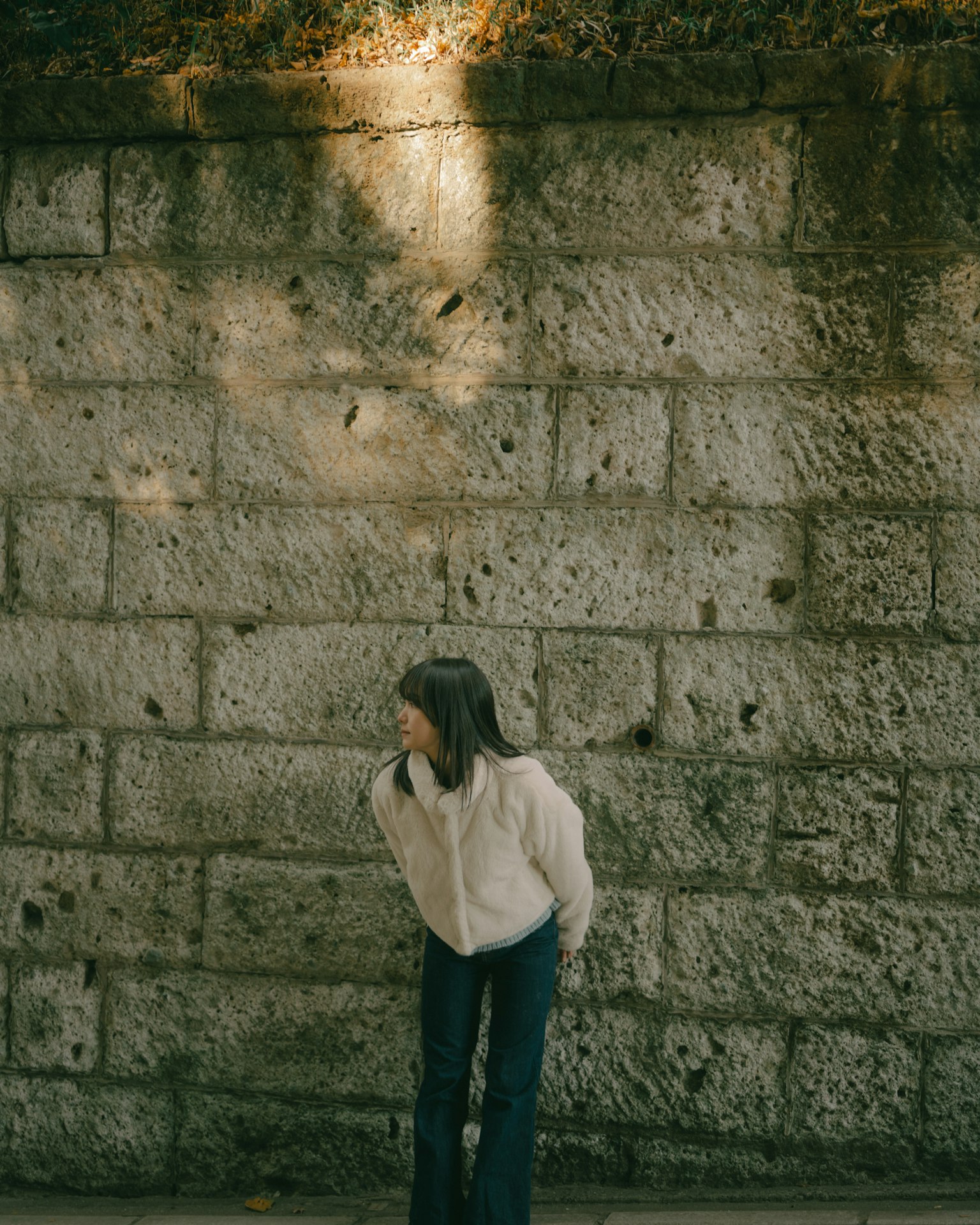Una niña de pie frente a una pared de piedra con luz suave iluminándola