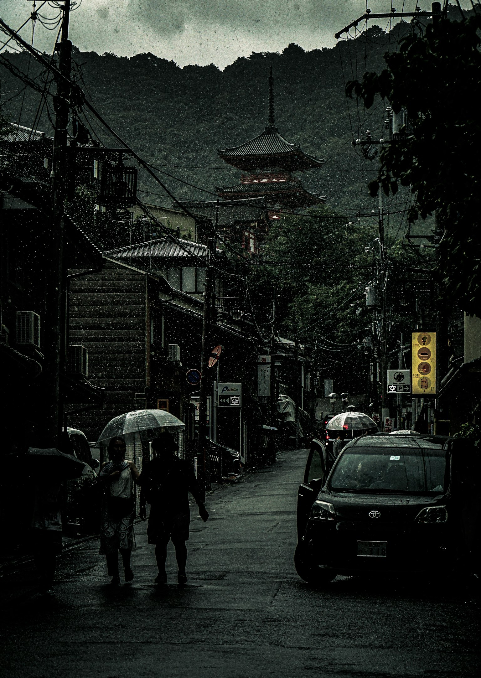 Calle estrecha bajo la lluvia con una torre en el fondo montañoso