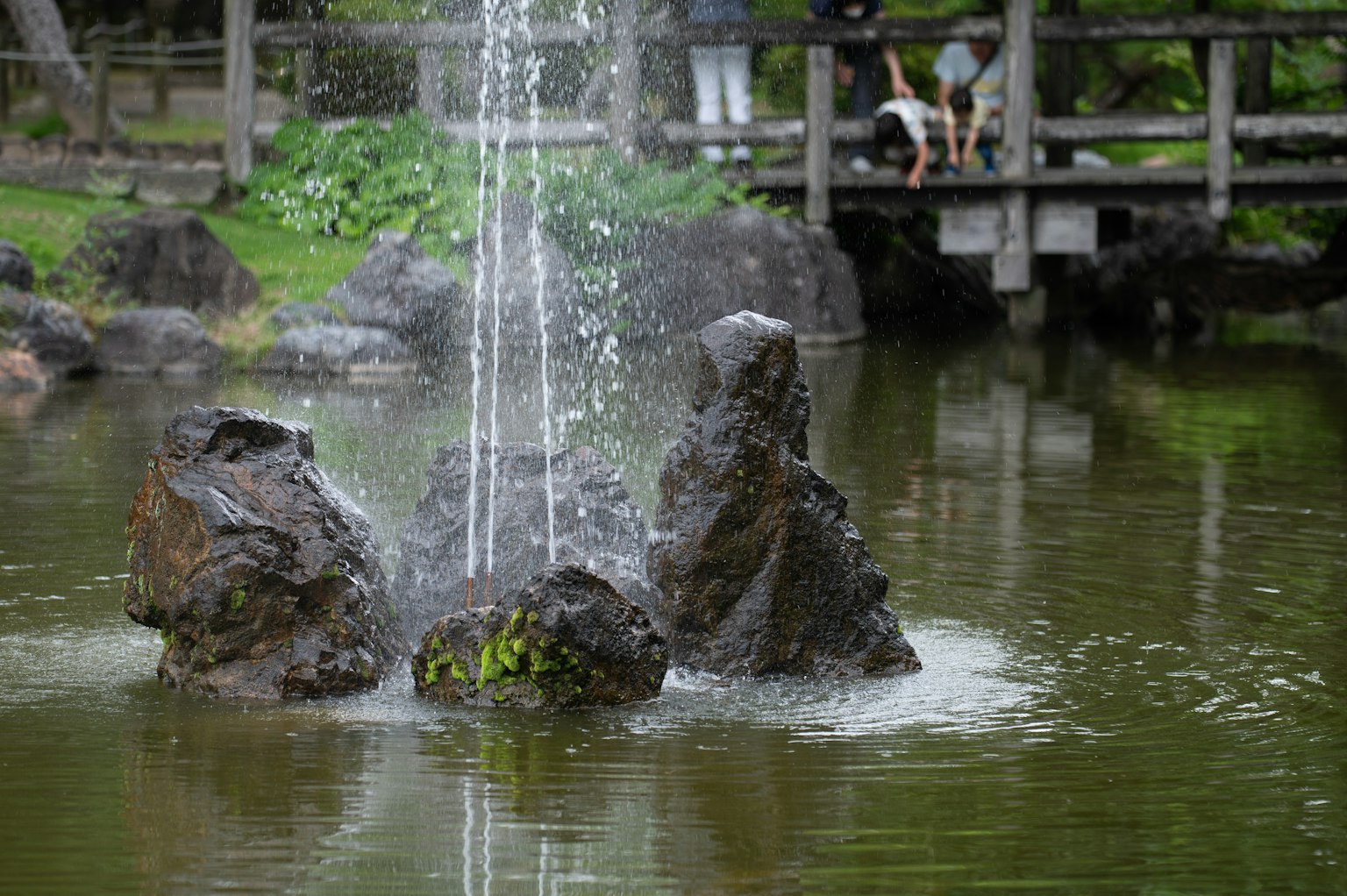 Fontaine d'eau jaillissant des rochers dans un étang entouré de verdure